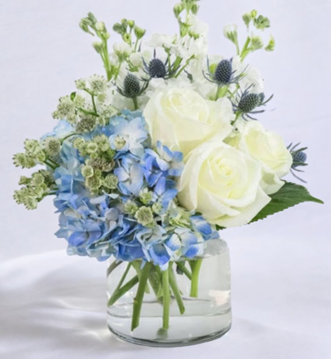 Blue Moonlight Serenade - This arrangement capture the serene and elegant combination of blue hydrangeas, white roses, white stock, blue thistle, white astrantia, and greenery in your arrangement. They evoke a sense of calmness, beauty, and natural harmony.