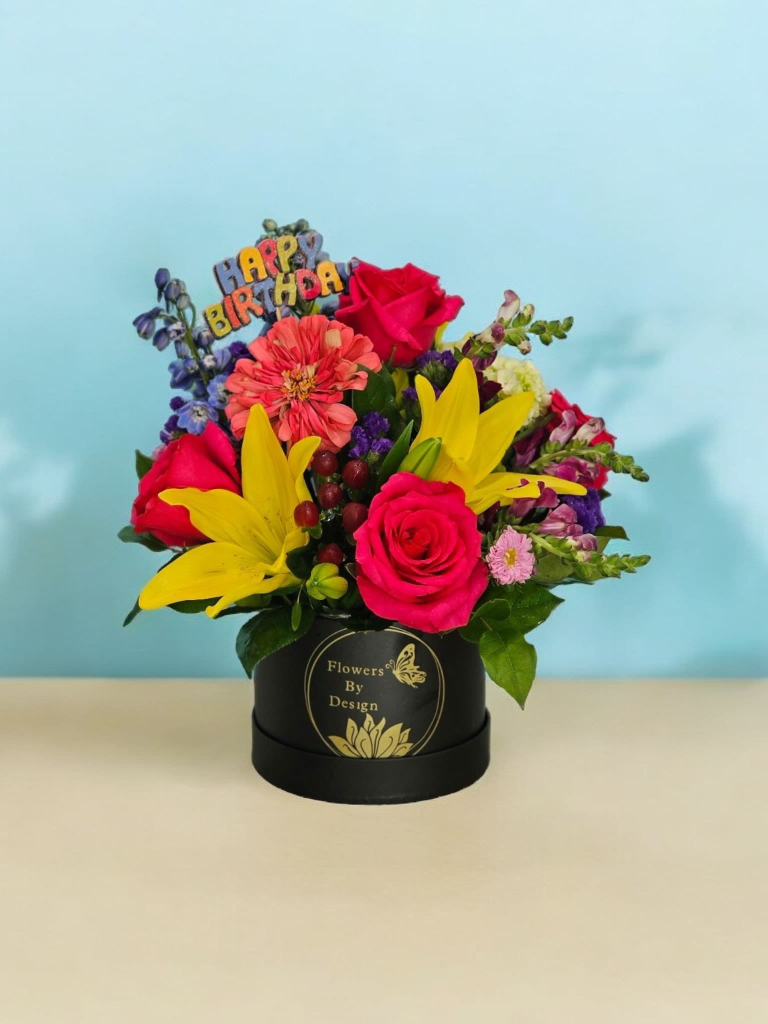 Midnight Blossom Symphony. - This name reflects the contrast of the black box with the vibrant colors of hot pink roses, yellow lilies, blue delphinium, red hypericum, pink Matsumoto, purple snapdragon, and hot pink dahlias. The addition of greenery and purple filler completes the arrangement, creating a harmonious and striking composition reminiscent of a rich and colorful symphony against a midnight backdrop.