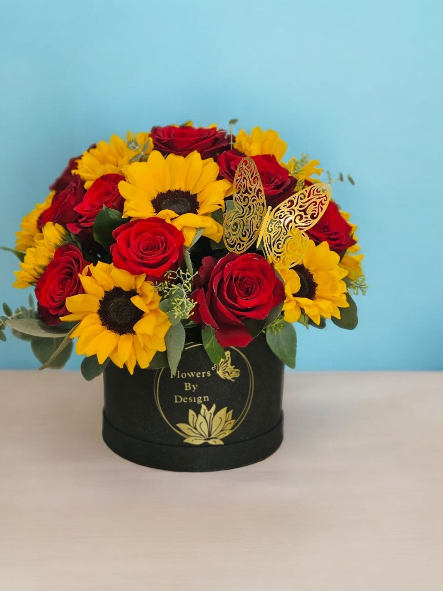 Scarlet Sunflower Serenade - This Arragement combines the boldness of the red roses with the warmth of the sunflower, set against the contrast of the black box. The greenery and fine filler add a touch of elegance and completeness to the arrangement, making it a striking and memorable composition.
