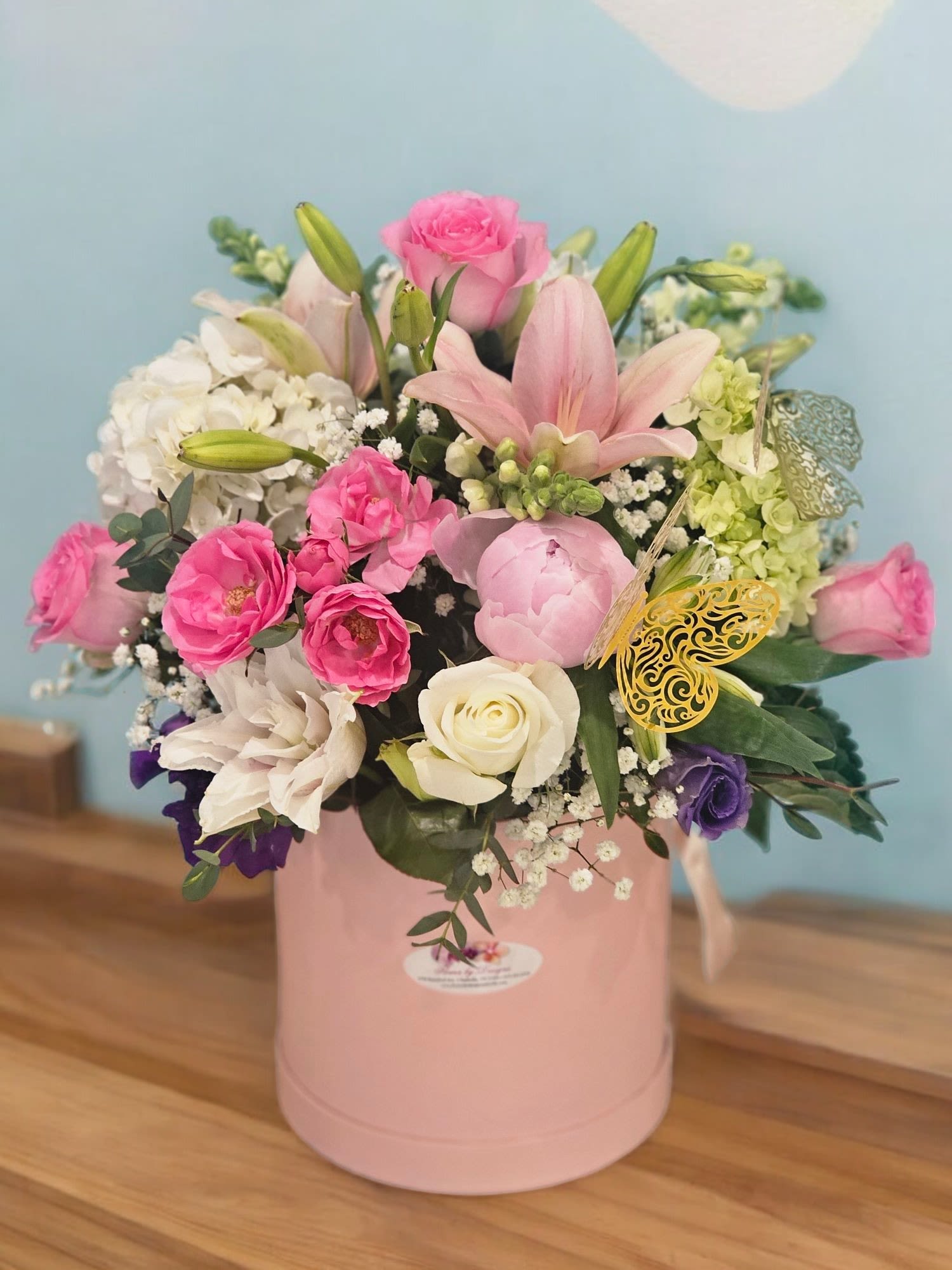 Pink Blossom Melody - this lovely arrangement captures the harmonious blend of pink hues with touches of white and purple, featuring spray roses, lilies, peonies, roses, hydrangeas, snapdragons, and lisianthus. The greenery and fine filler enhance the composition, creating a beautiful melody of colors and textures within the pink box.
