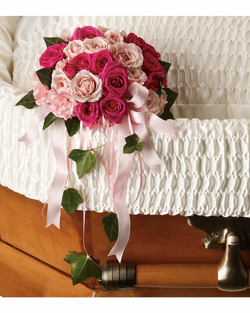 Pink rose casket bouquet with satin ribbons resting on a white lined casket