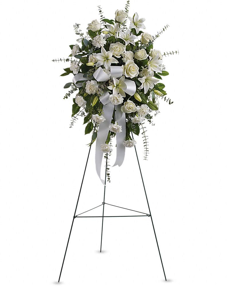 Standing spray of white lilies, roses, and carnations with a white ribbon on a metal easel.