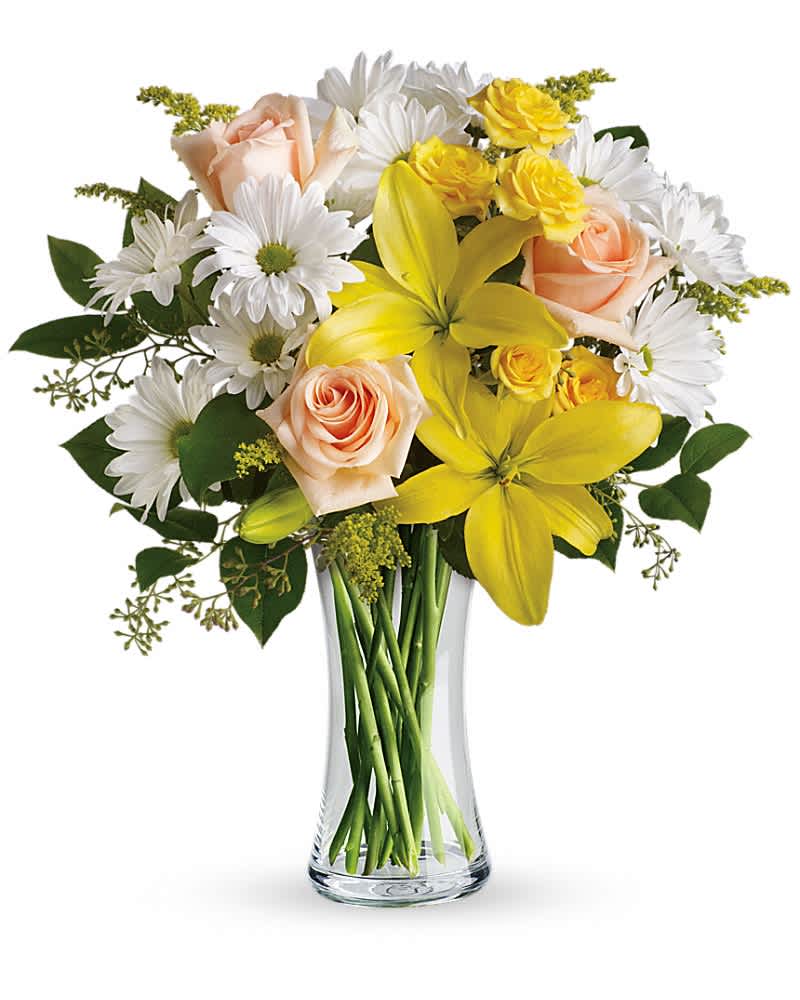 Mixed bouquet of yellow lilies, white daisies, and peach roses in a clear glass vase