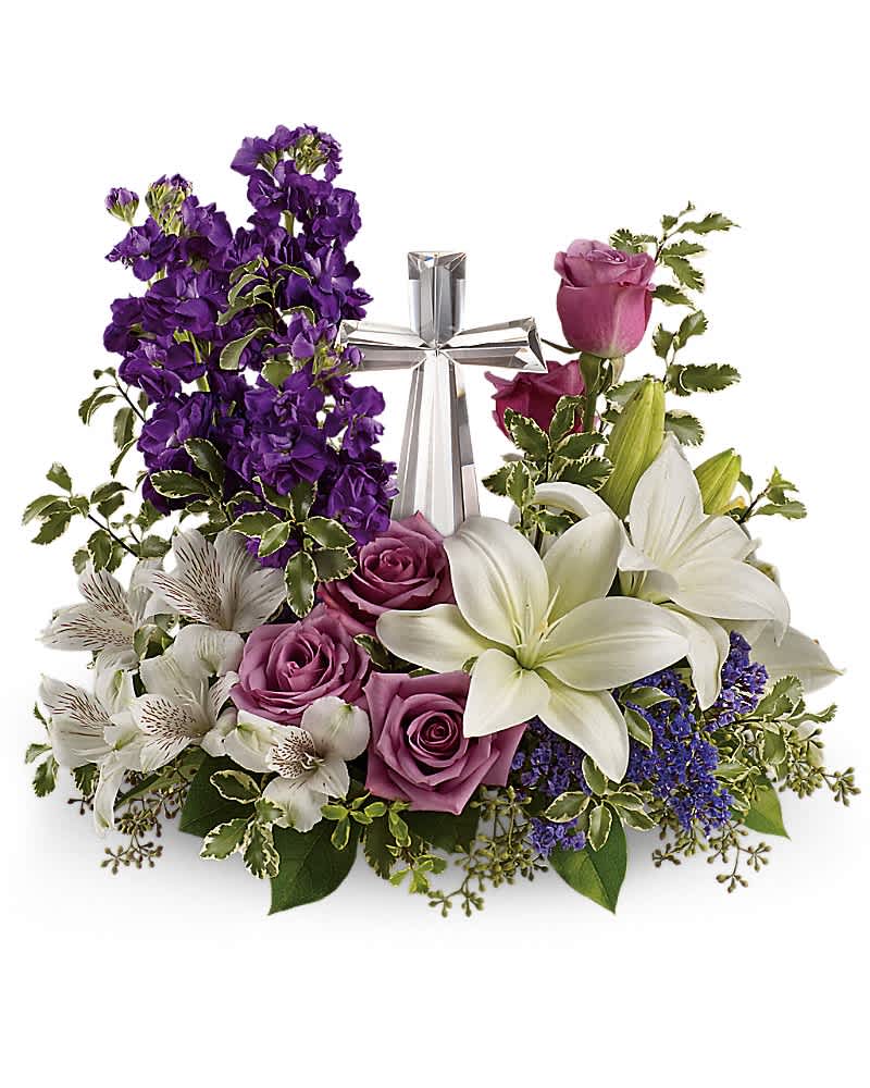 Low arrangement of white lilies, lavender roses, and purple flowers surrounding a clear glass cross