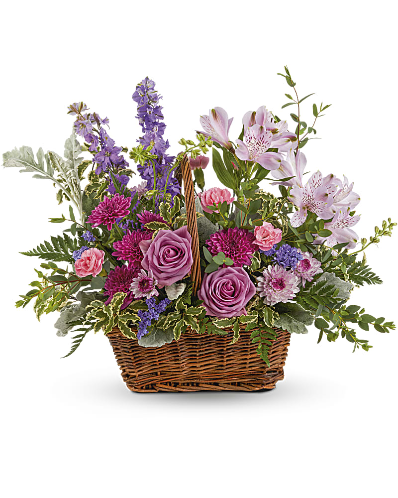 Wicker basket filled with pink roses, carnations, mums, and purple flowers in a mixed arrangement