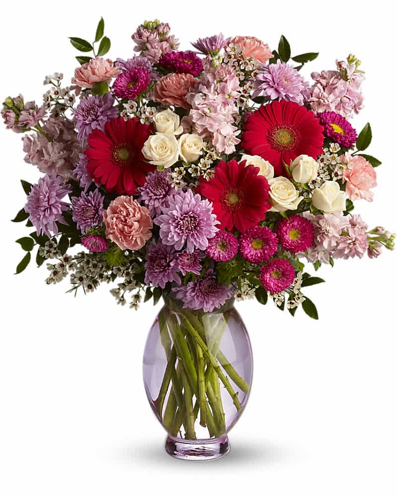 Mixed bouquet of pink and purple blooms with cream roses in a clear glass vase