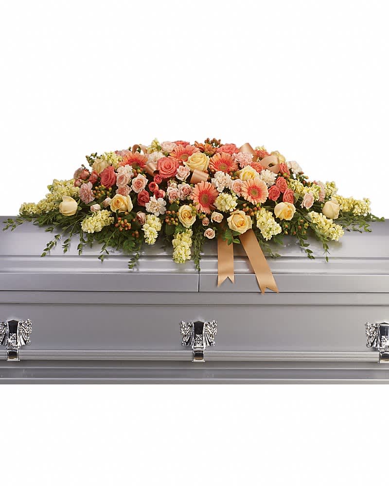 Pastel peach and yellow casket spray of roses and gerbera daisies on a silver casket