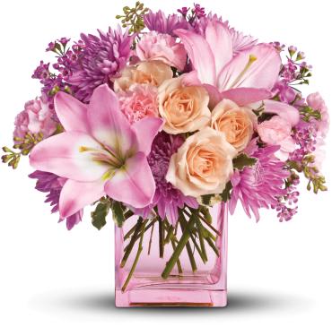Pink lilies, roses, carnations, and mums arranged in a pink rectangular glass vase
