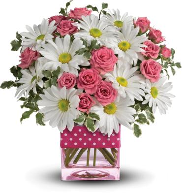 Arrangement of white daisies and pink roses in a glass cube vase with a pink polka-dot ribbon.