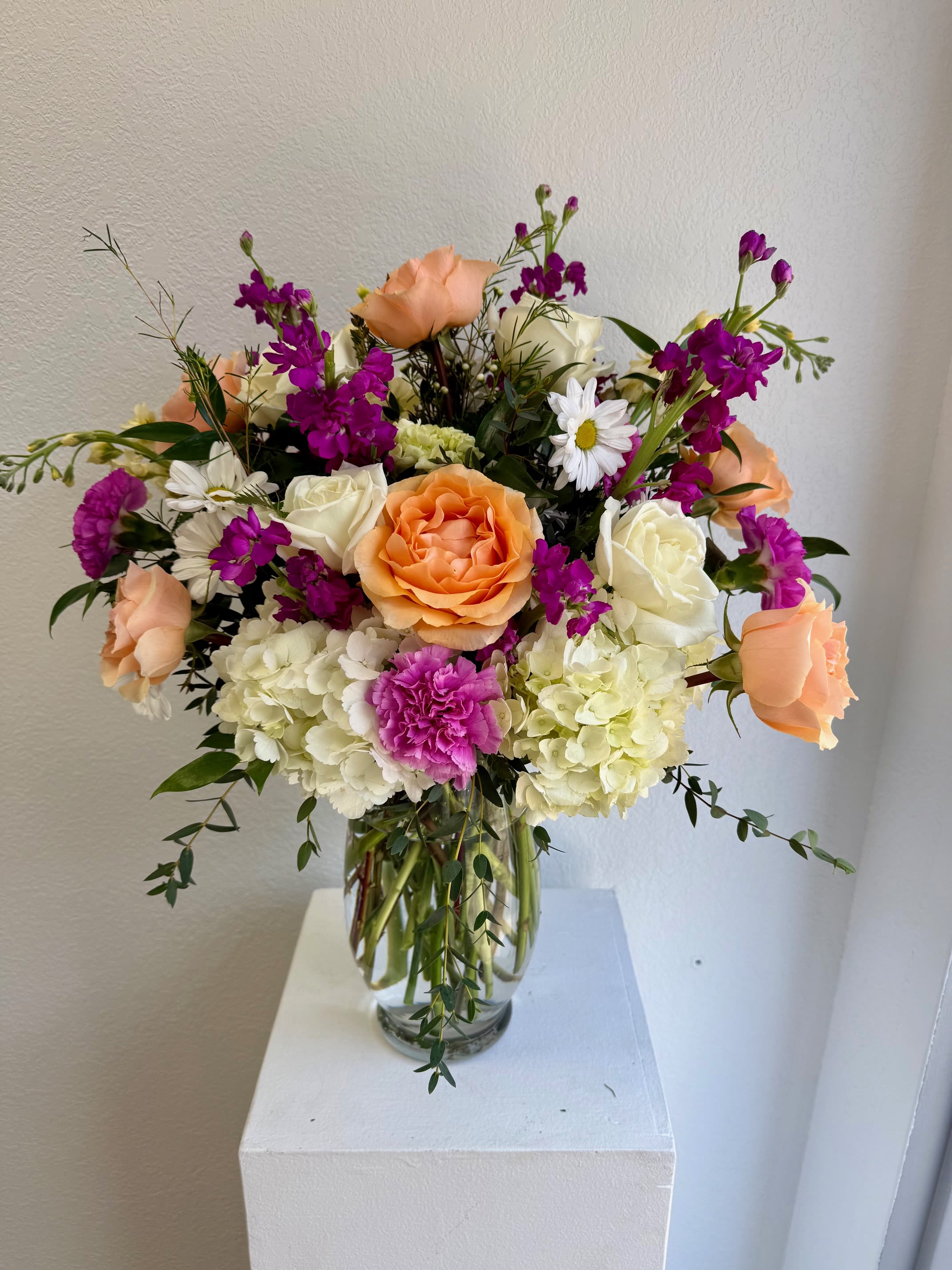 Blossom Rhapsody - A joyful flourish in our Symphony in Bloom Collection, Blossom Rhapsody is a lush arrangement bursting with vibrant seasonal blooms. Layers of fresh florals create a lively harmony of color and texture, blending garden favorites into a design that feels abundant, romantic, and full of life. With hydrangea, roses, daisies and other seasonal blooms. 