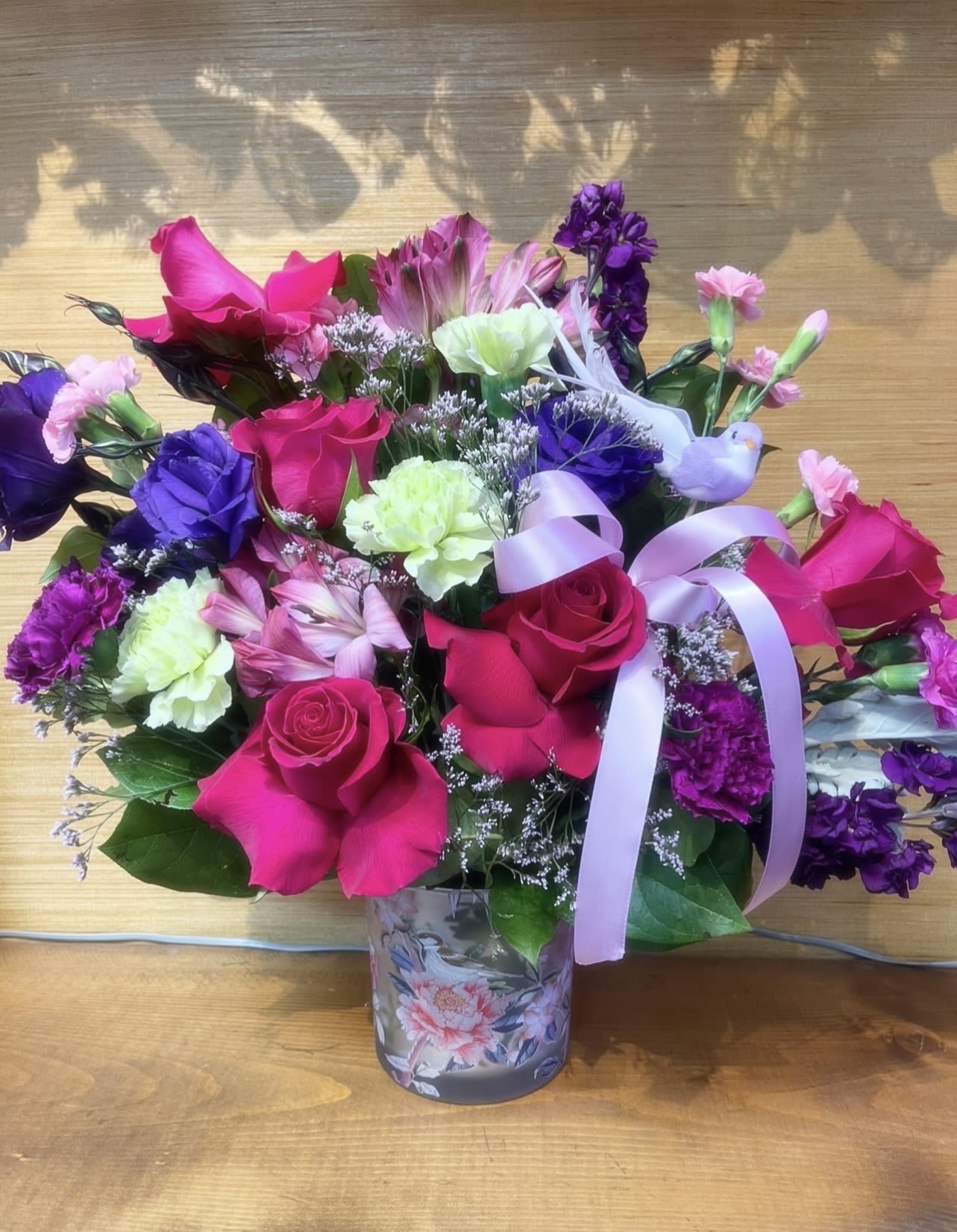 BIRDSONG - FRESH FLOWERS, ROSES, CARNATIONS, MINI CARNATIONS ETC. DESIGNED IN AN COLORED GLASS VASE WITH BIRDS AND BUTTERFLIES.