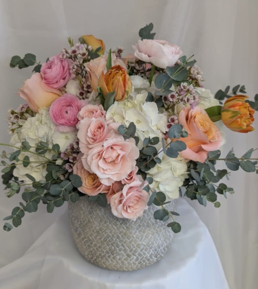 Round arrangement of blush roses, white hydrangeas and pink ranunculus in a textured gray ceramic vase
