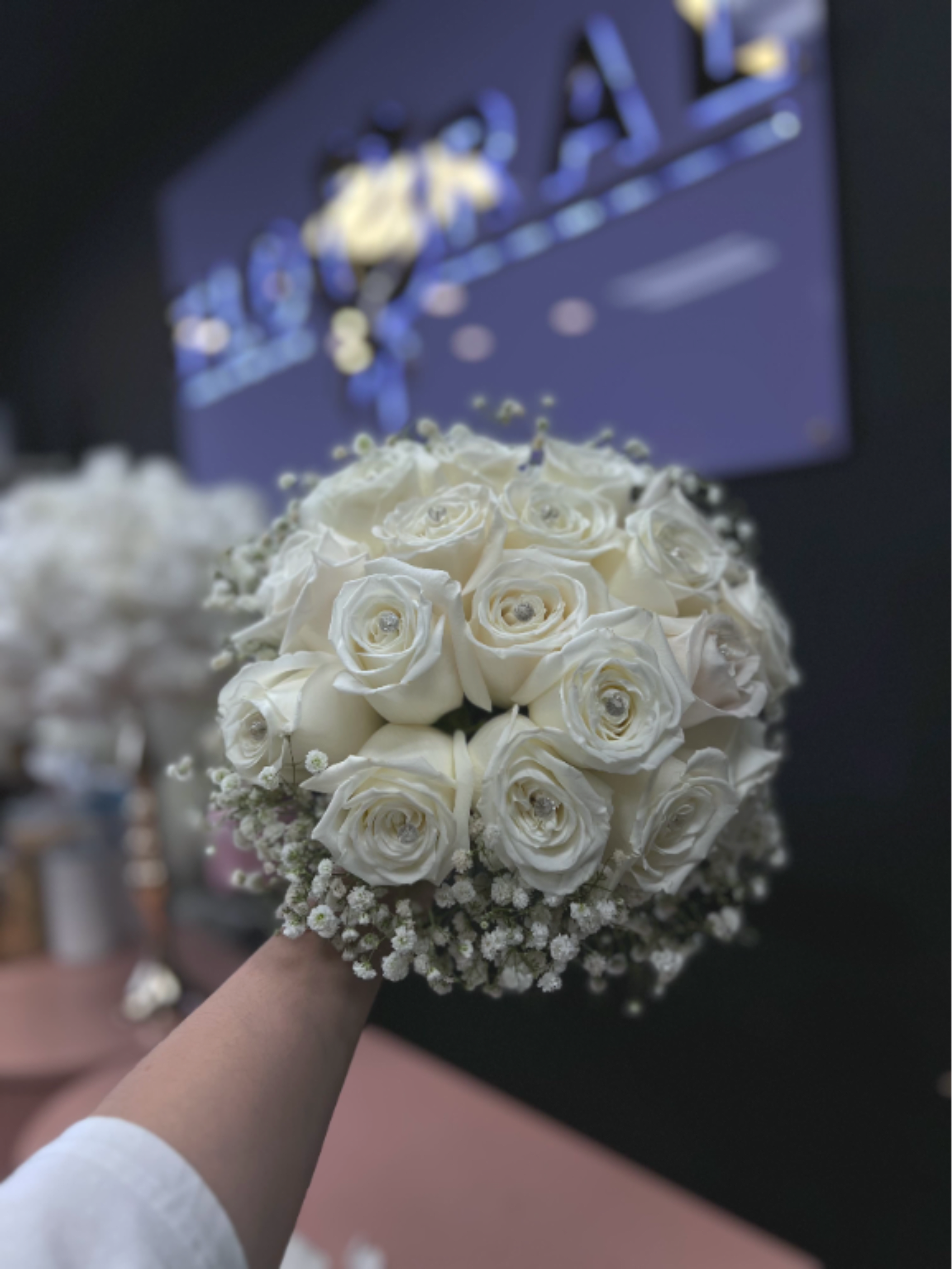 Round bridal bouquet of white roses and baby's breath held in front of a dark background