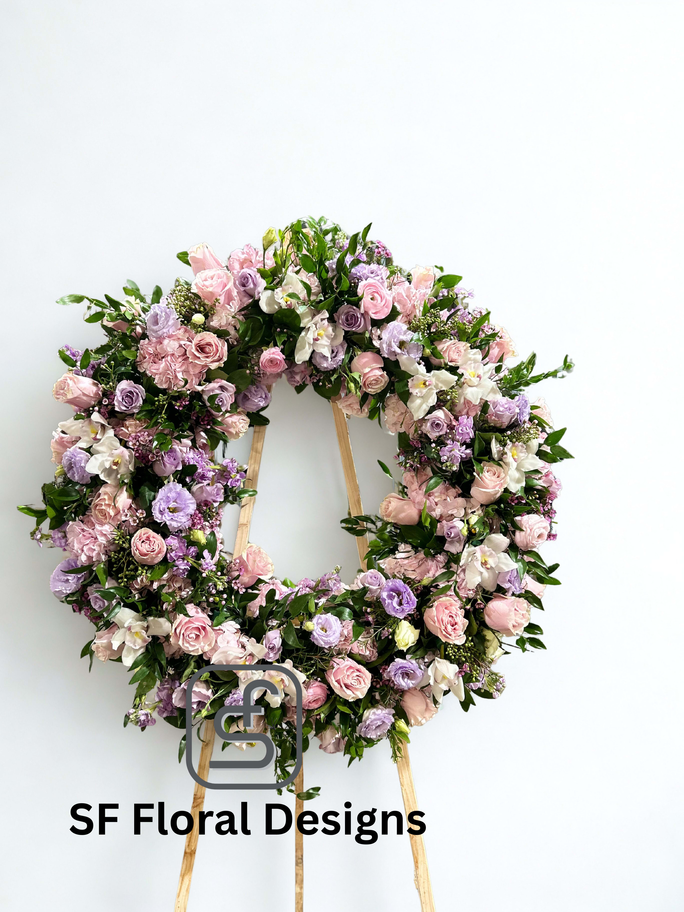 Standing wreath of pink and lavender roses and lisianthus on a wooden easel against a white background