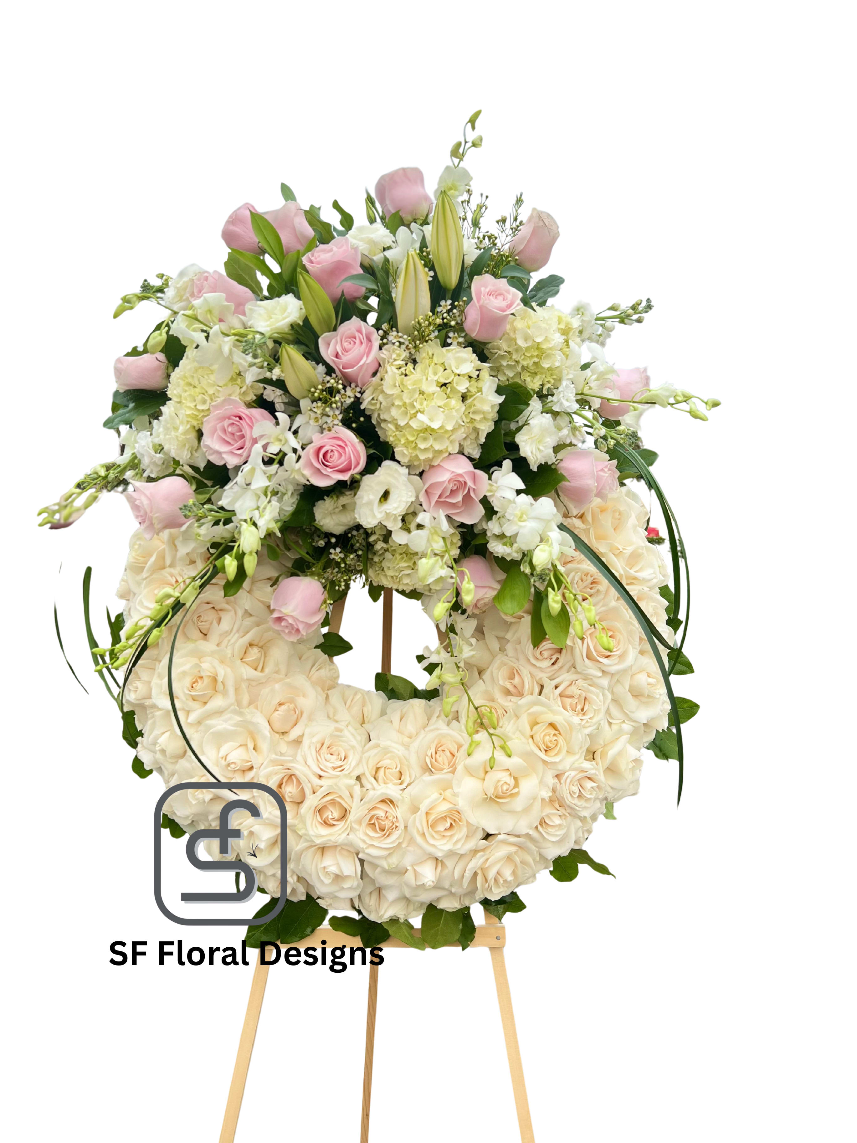 Large ivory rose wreath with pink roses, lilies, and white blooms arranged on top, displayed on a wooden easel.
