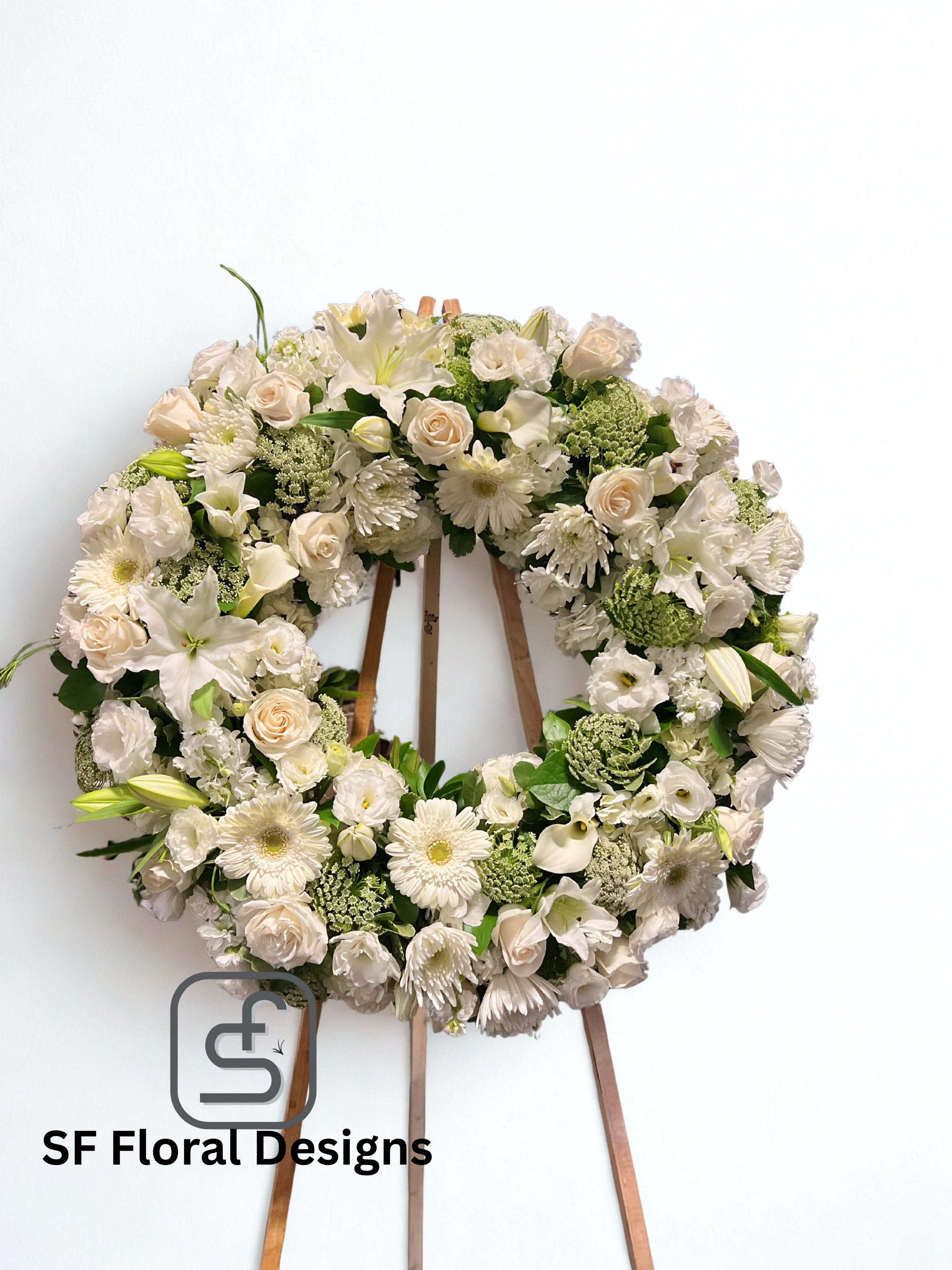 Large white and cream floral wreath with roses, lilies, and gerbera daisies on a wooden easel.
