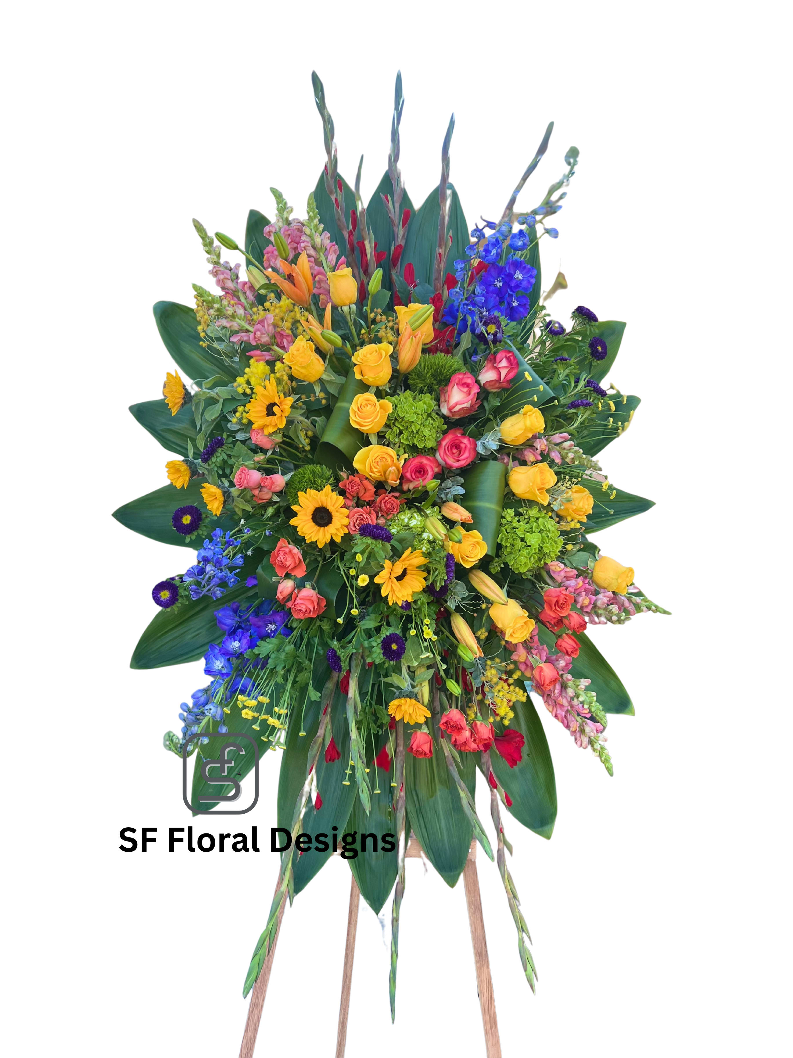 Tall multicolor standing spray with roses, lilies, delphinium, gerbera daisies, and snapdragons on a wooden easel.