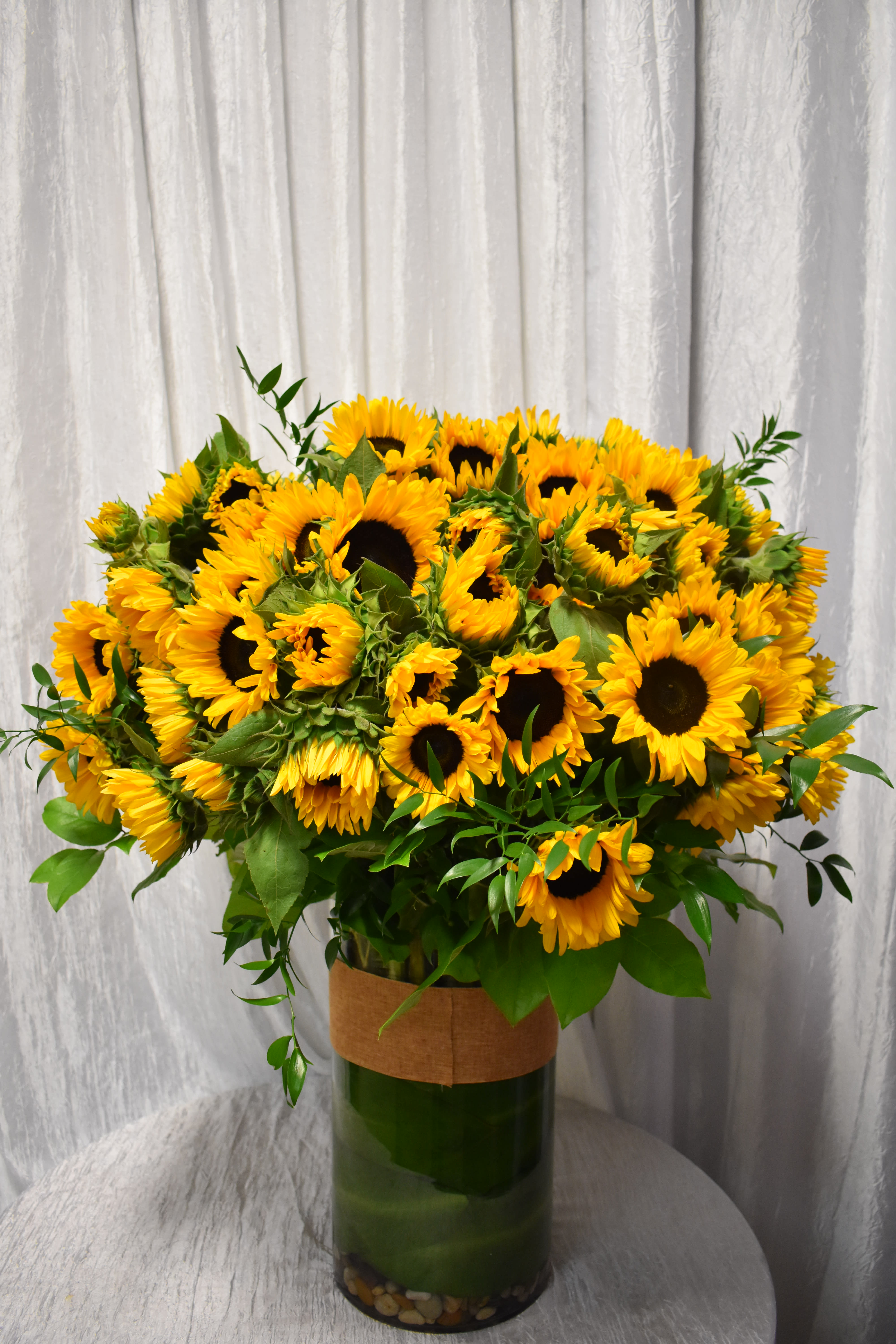 Large arrangement of yellow sunflowers in a tall clear glass vase on a table