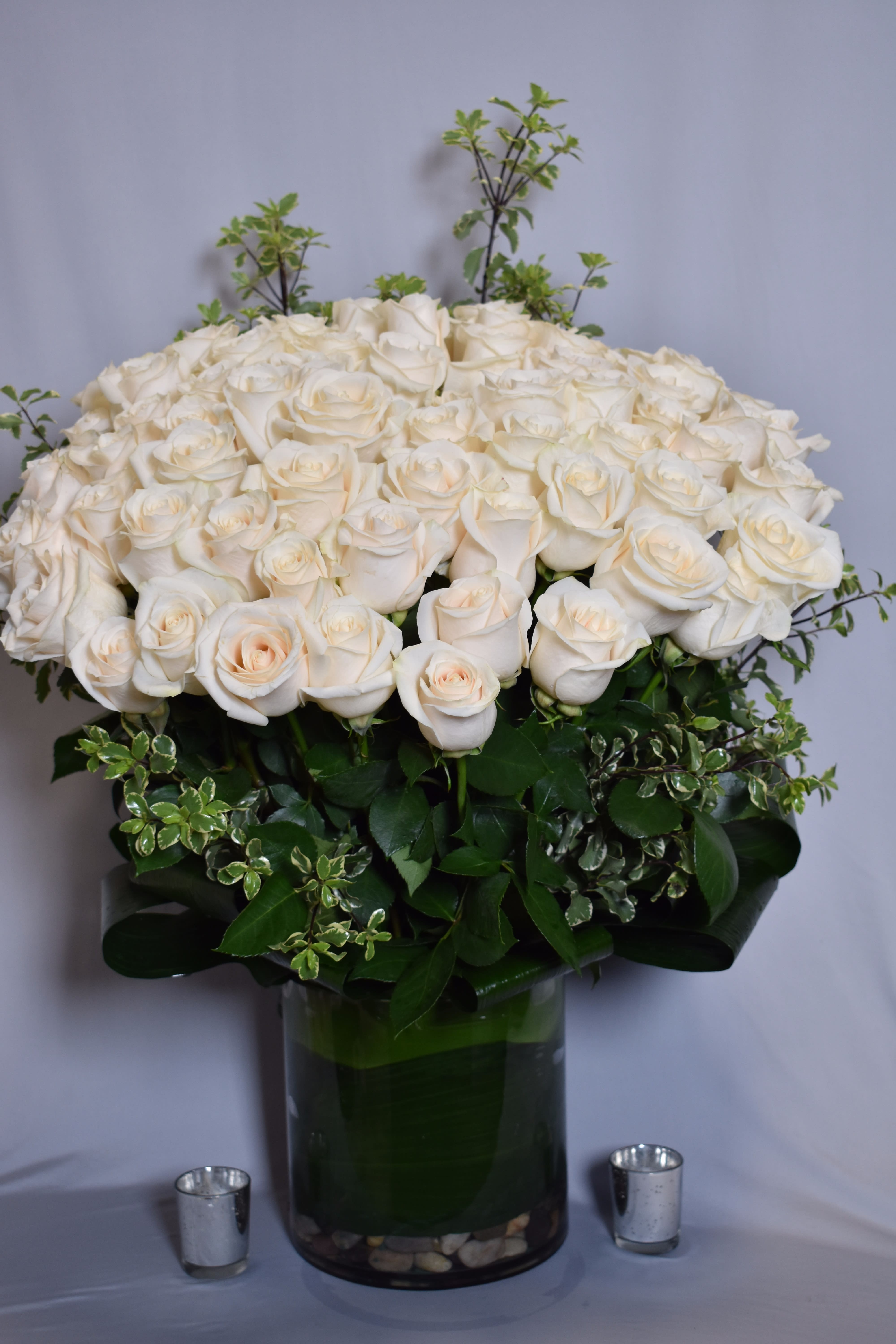 Large arrangement of ivory roses with decorative foliage in a clear glass cylinder vase.