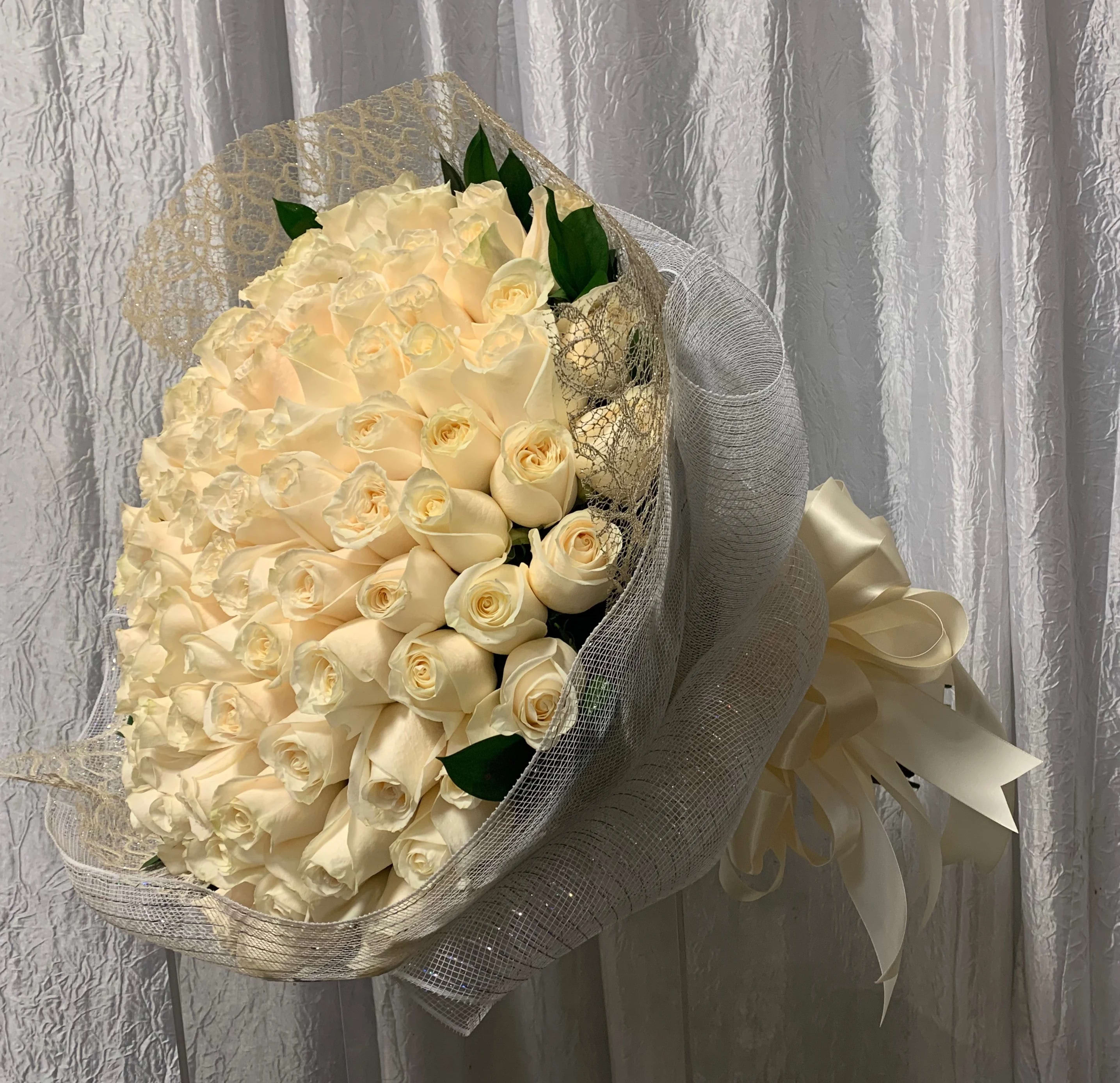 Large hand-tied bouquet of cream roses wrapped in white mesh with an ivory ribbon bow