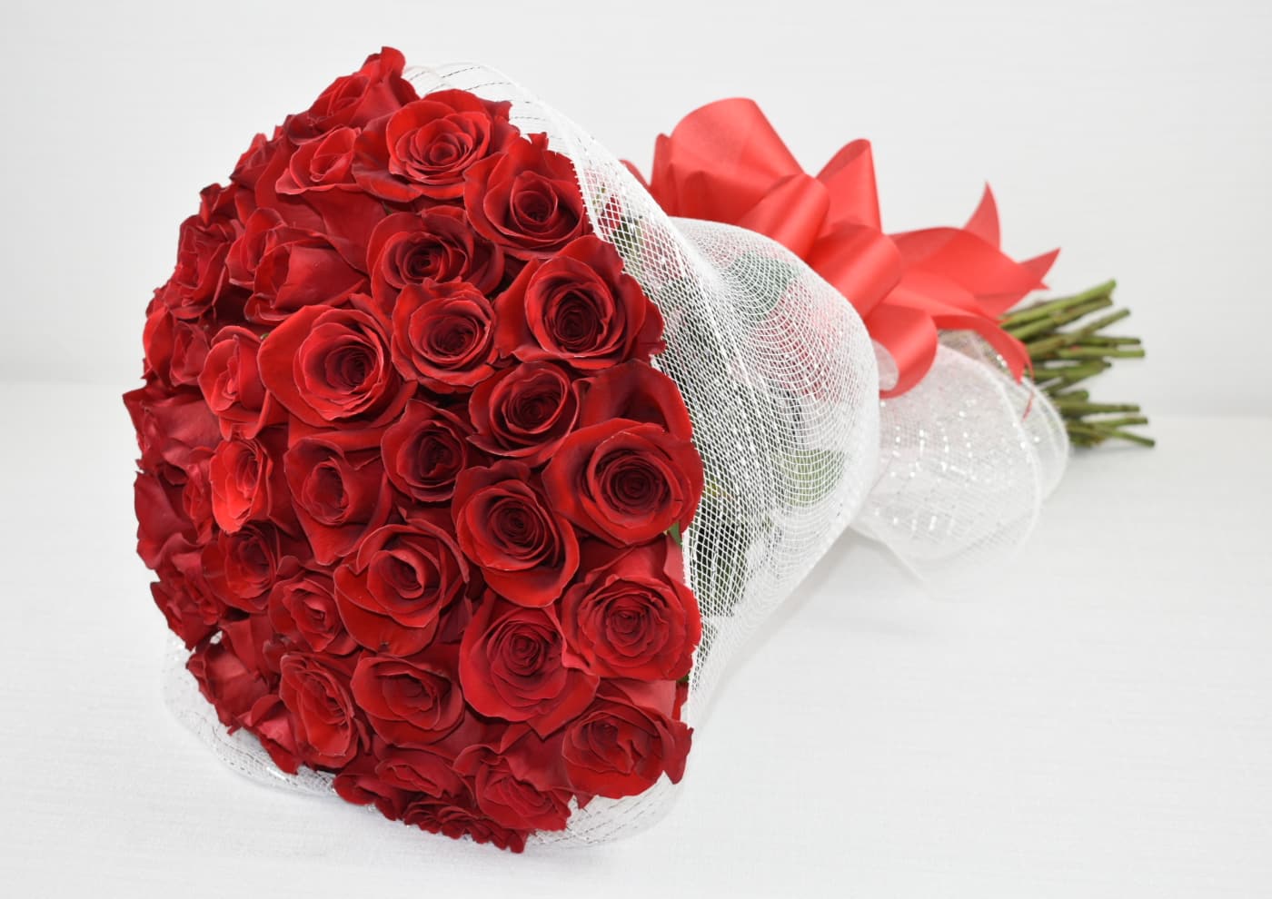 Large bouquet of red roses wrapped in white mesh with a big red bow.