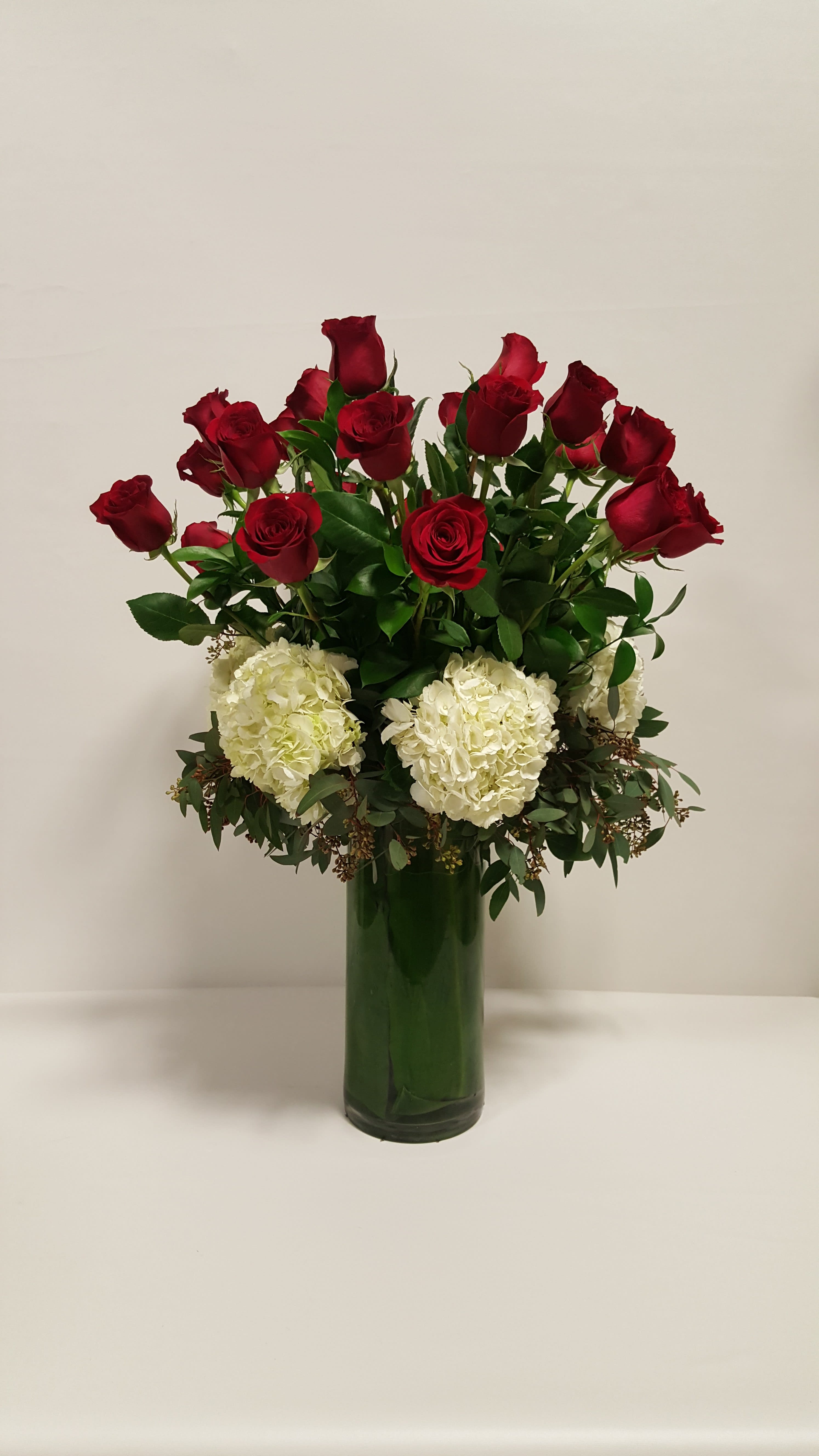 Tall arrangement of red roses and white hydrangeas in a clear green-lined glass vase