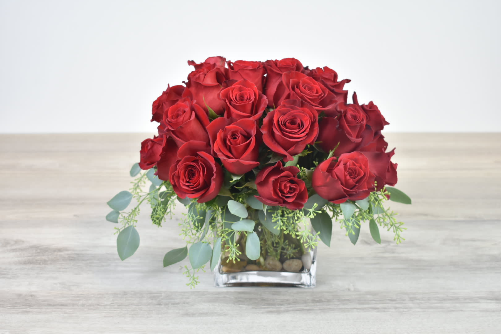 Low arrangement of red roses in a clear glass cube vase with trailing greenery