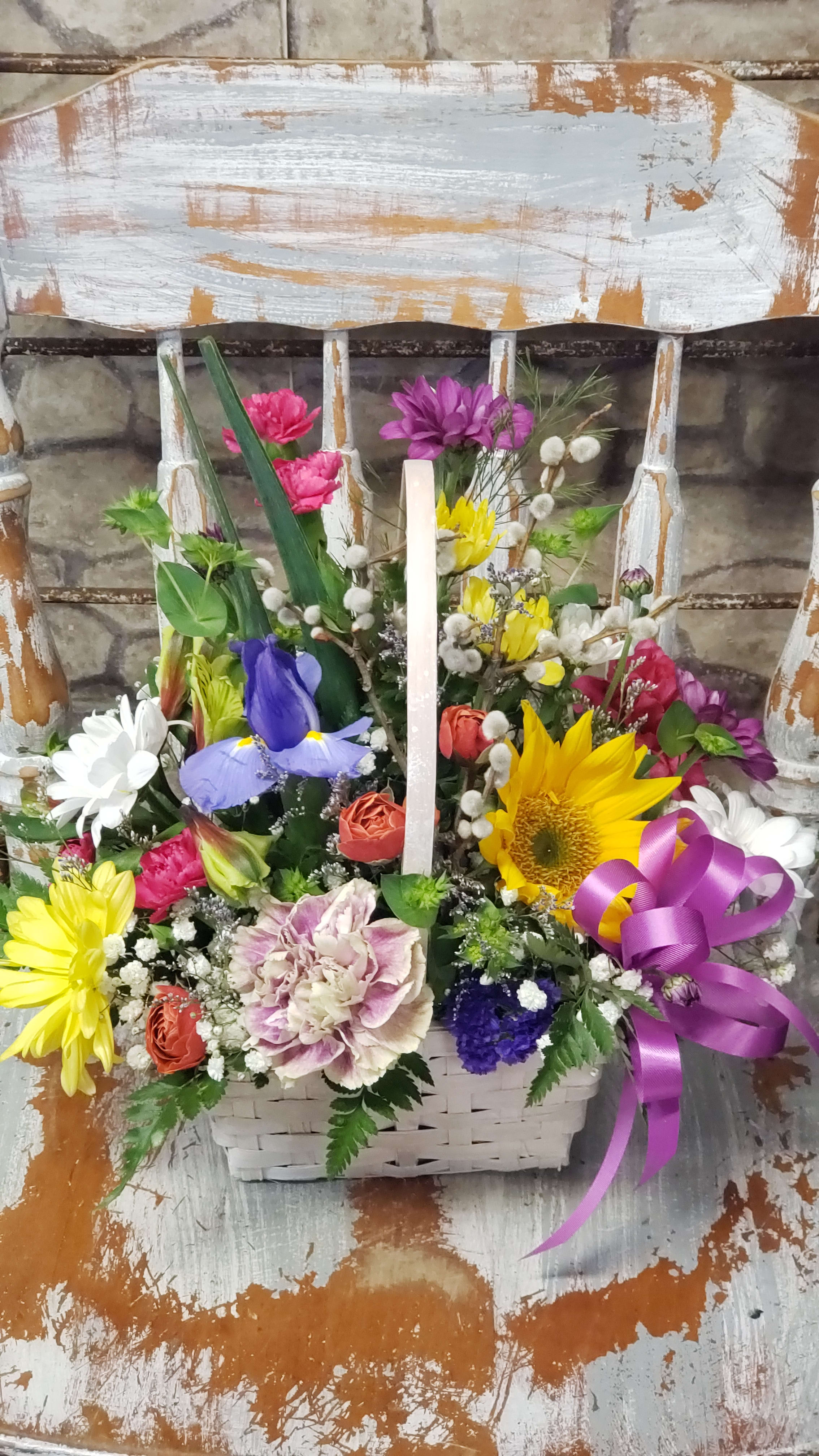 Colorful mixed flower basket with sunflower, iris, daisies, and a purple ribbon bow