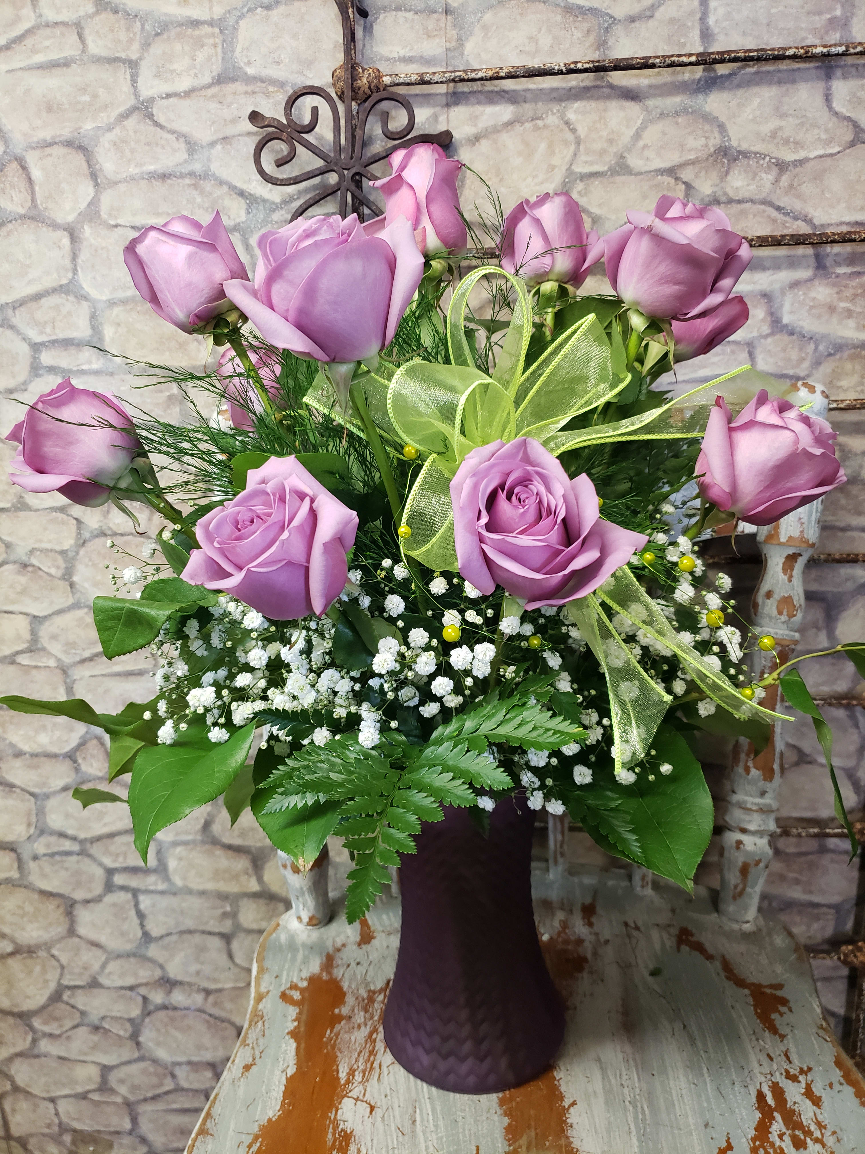 Lavender roses with baby's breath in a purple vase with a light green ribbon bow