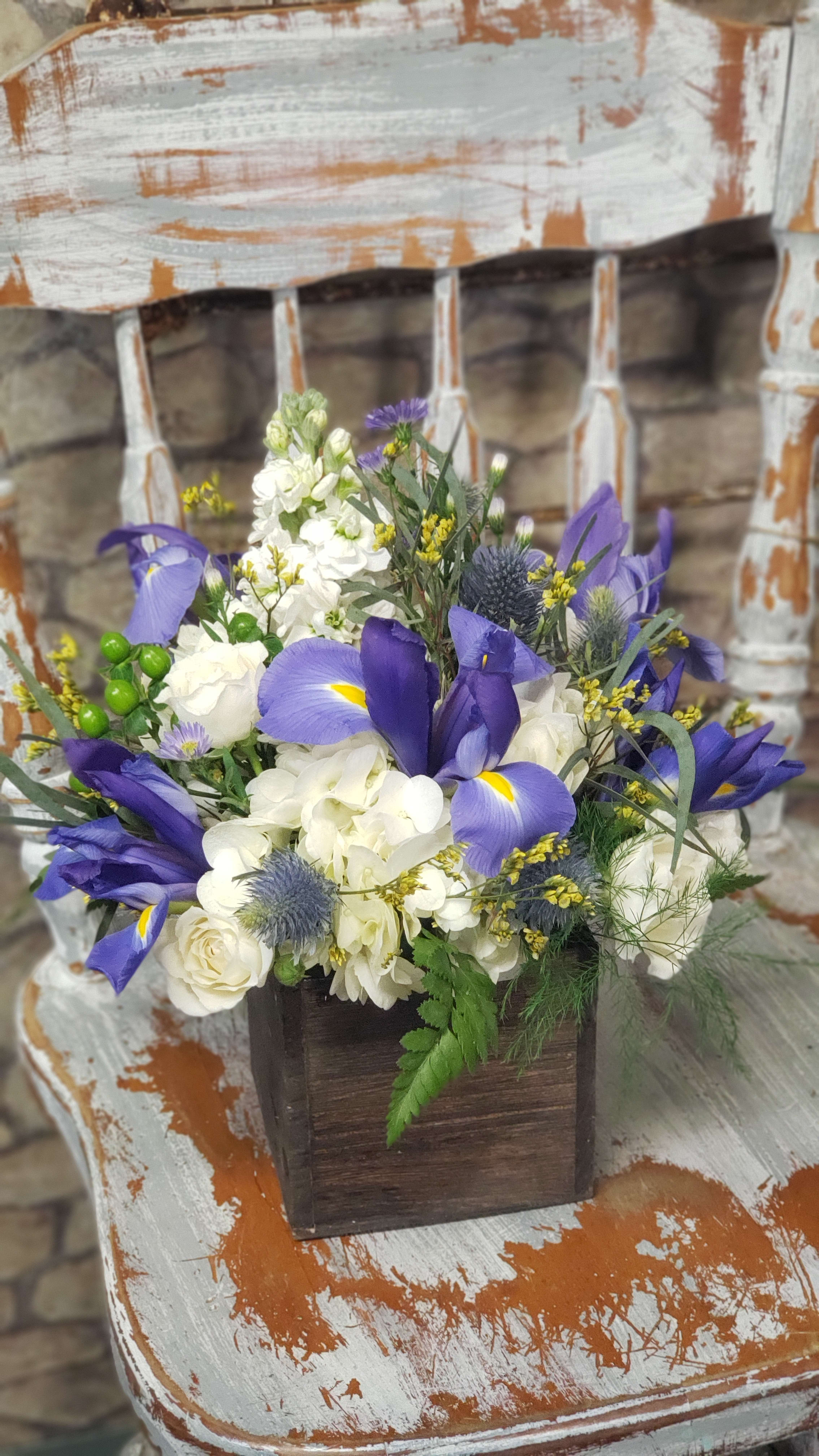 Purple irises and white hydrangeas in a rustic wooden box arrangement on a distressed chair