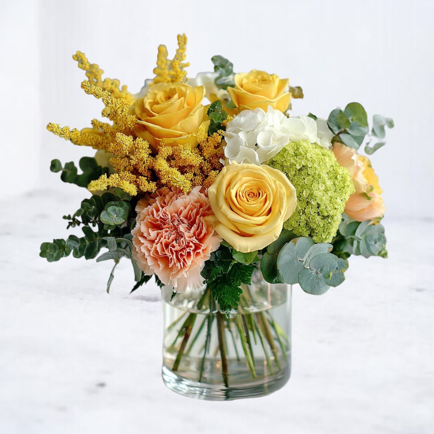 Solar Thicket - Bursting with warmth and woodland whimsy, Solar Thicket brings together the golden glow of yellow roses, the fresh charm of green hydrangeas, soft blush carnations, and the silvery shimmer of eucalyptus. Nestled in a modern cylinder vase, this compact yet radiant arrangement is a celebration of light, color, and earthy elegance.  Perfect for brightening someone's day, offering congratulations, or just because—Solar Thicket is a small arrangement with a bold personality.