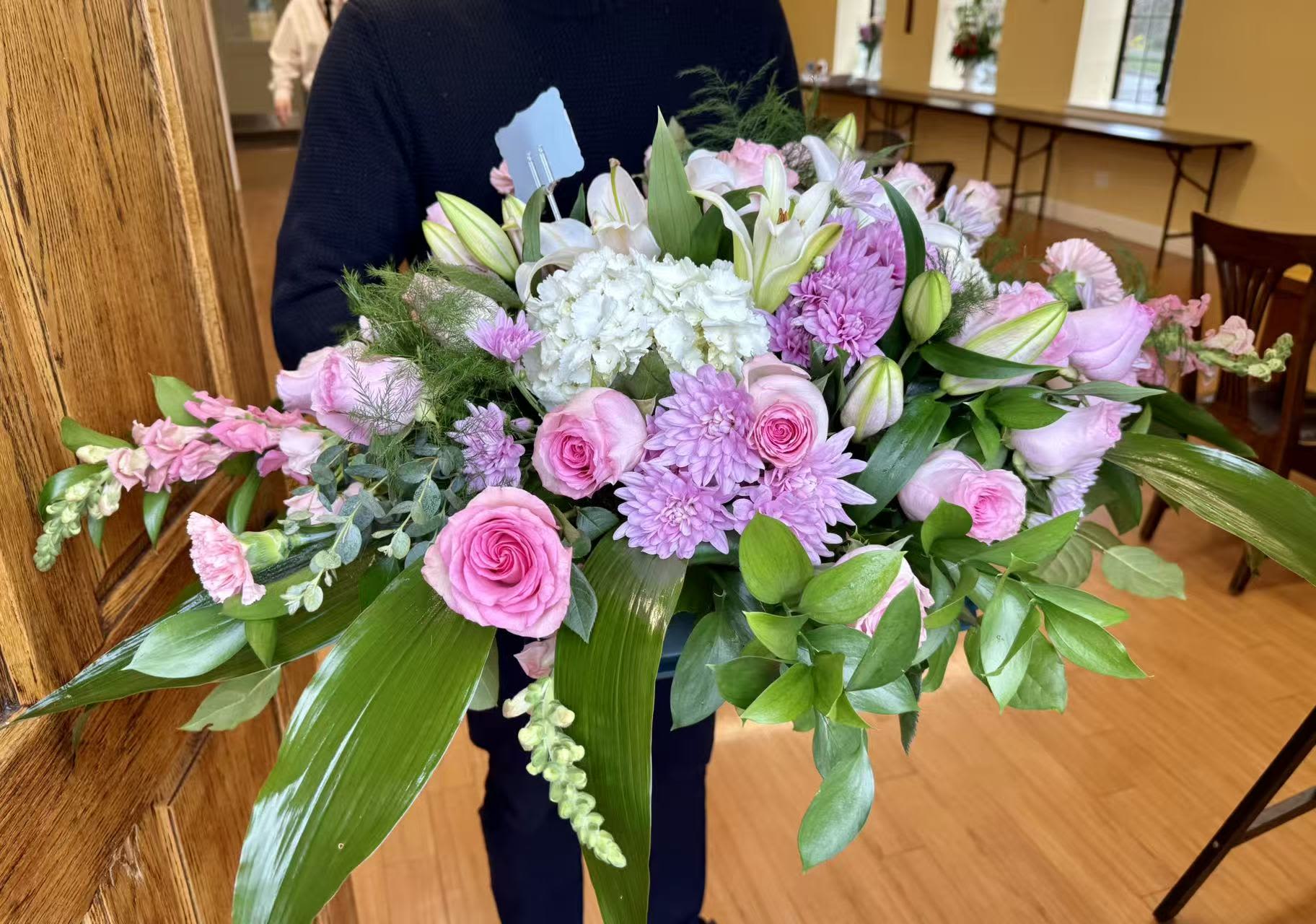 Heavenly Peace Casket Spray - A graceful casket spray designed in soft shades of pink and white, featuring premium pink roses, hydrangea, lilies, and seasonal blooms. Accented with lush greenery, this elegant arrangement expresses love, peace, and heartfelt remembrance. Designed to rest atop the casket, it creates a serene and beautiful tribute for a final farewell.