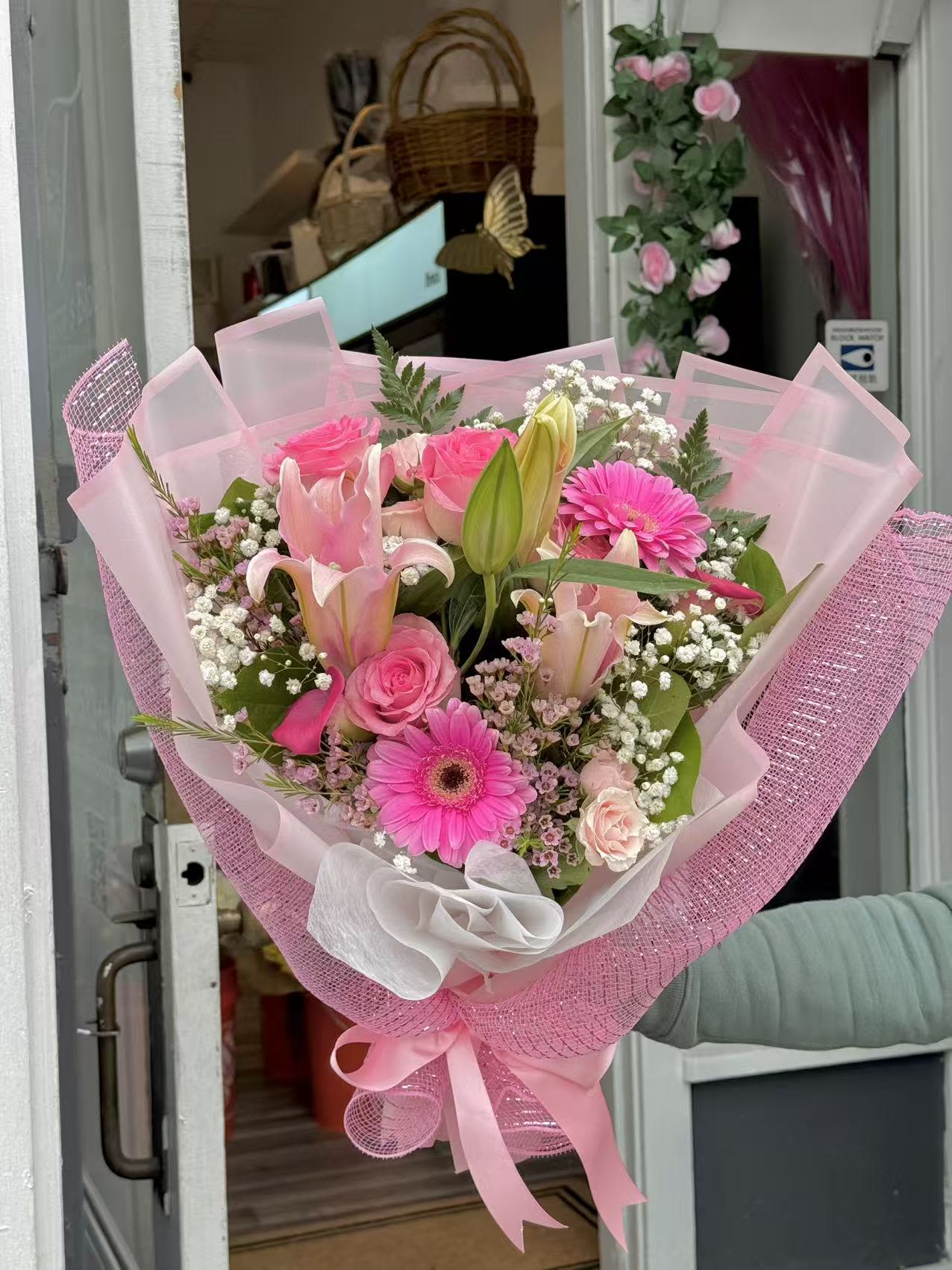 Sweet Blush Hand-Tied Bouquet - A charming hand-tied bouquet in soft blush tones, featuring pink roses, lilies, gerbera daisies, and delicate filler flowers, beautifully wrapped in elegant pink layers. This bouquet is designed to express love, appreciation, and joy—perfect for birthdays, celebrations, or just because.