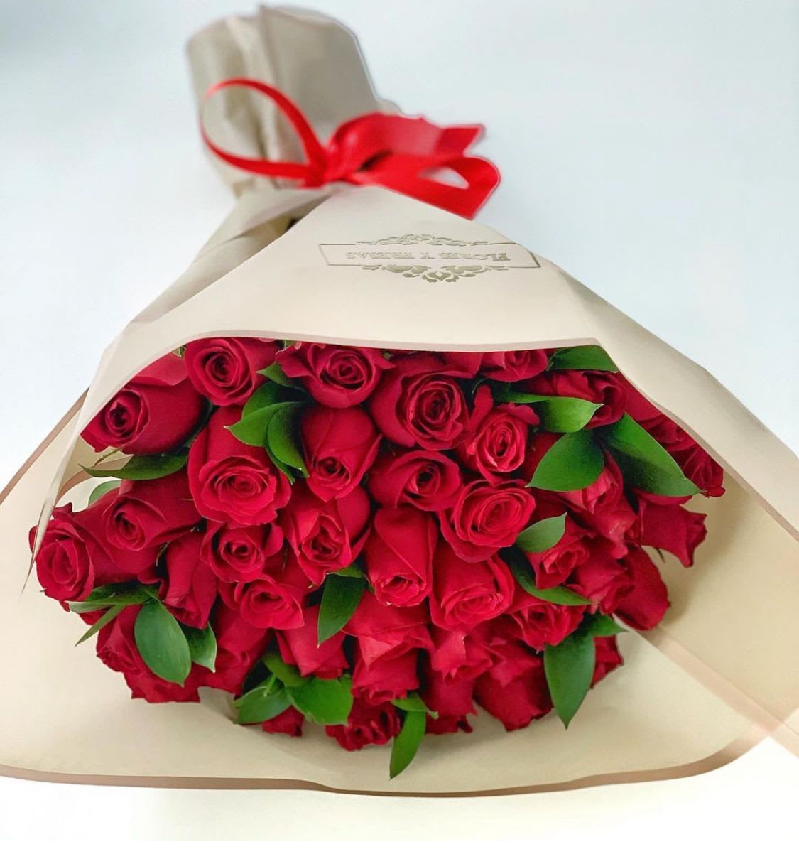 Large bouquet of red roses wrapped in cream paper and tied with a red ribbon