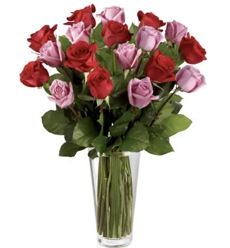 Tall bouquet of red and lavender roses in a clear glass vase