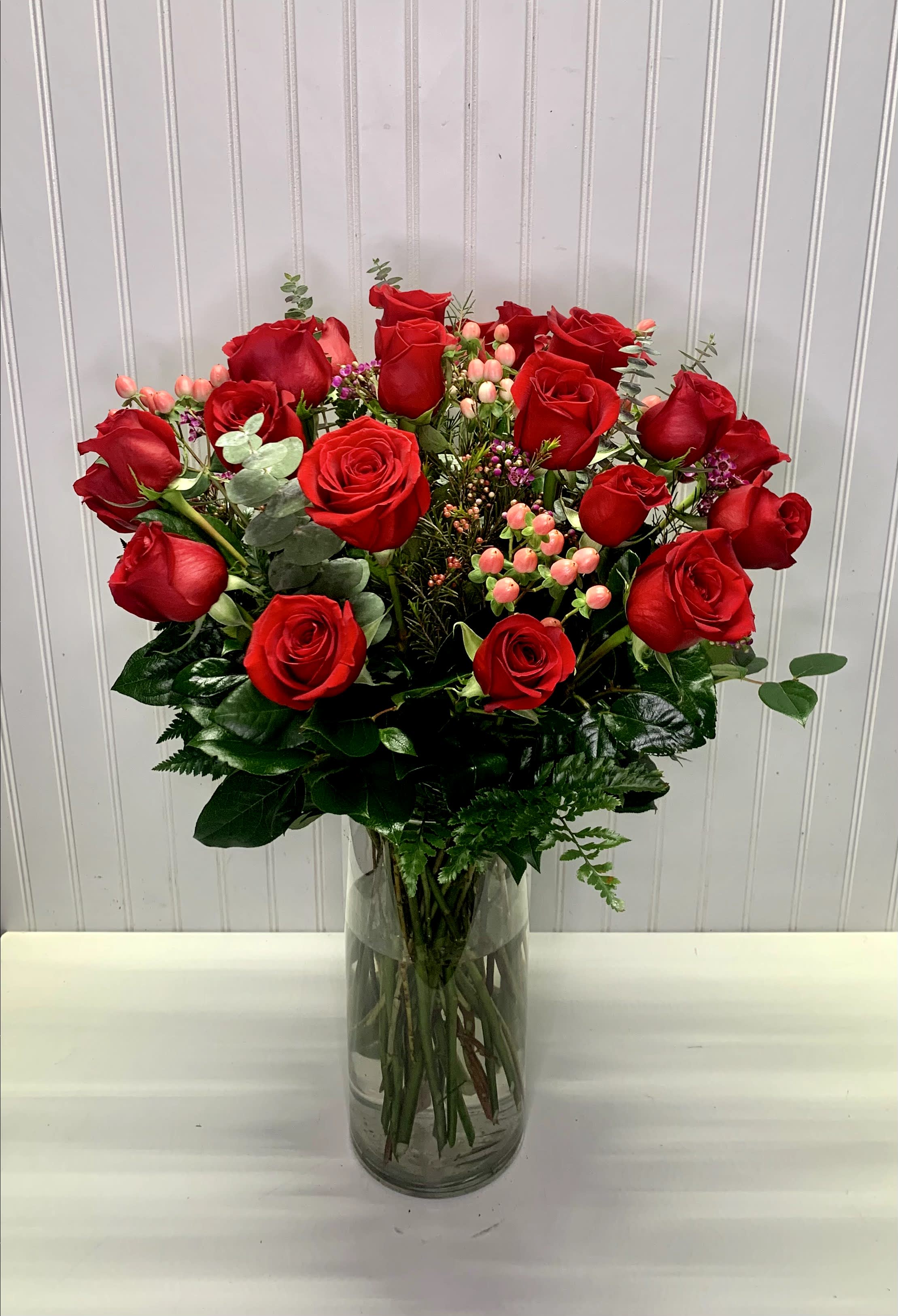 Tall arrangement of red roses with pink berries and filler flowers in a clear glass vase