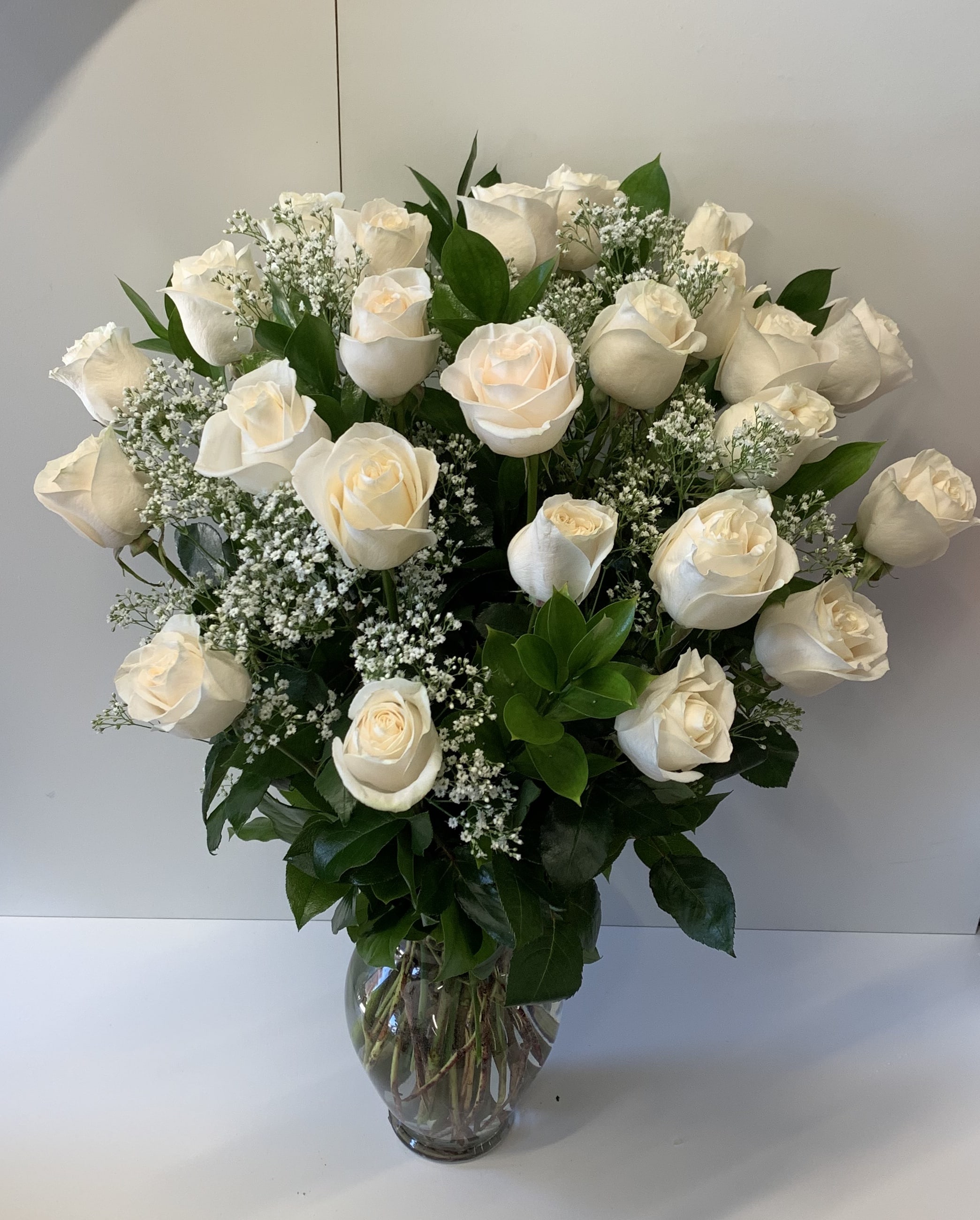 Tall arrangement of white roses with baby's breath in a clear glass vase
