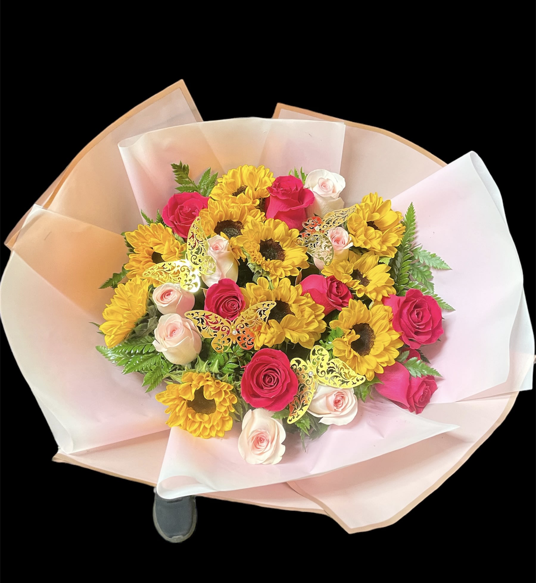 Round bouquet of yellow sunflowers with pink and ivory roses wrapped in soft pink paper
