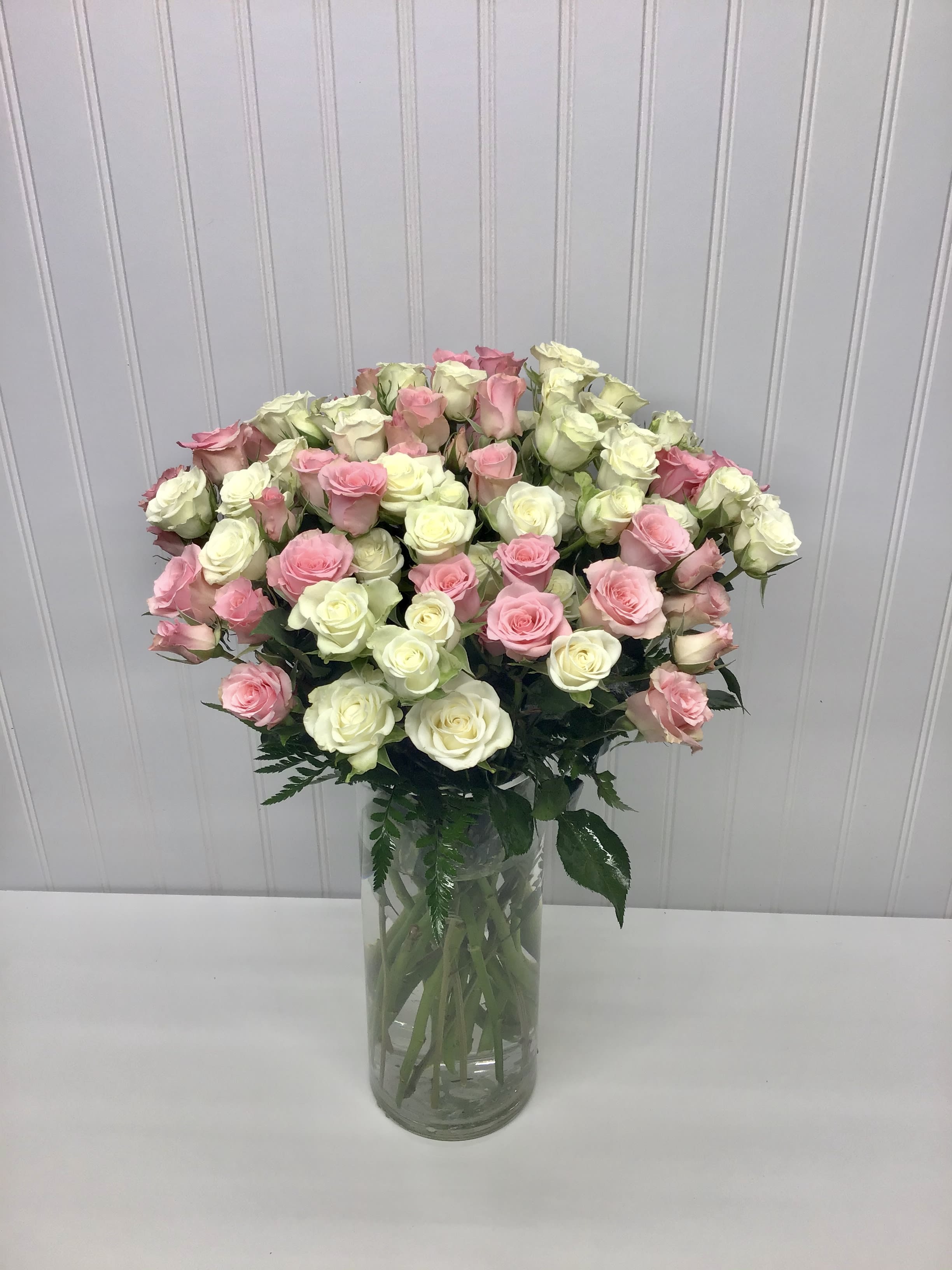 Tall clear vase of light pink and white roses arranged in a full, rounded display
