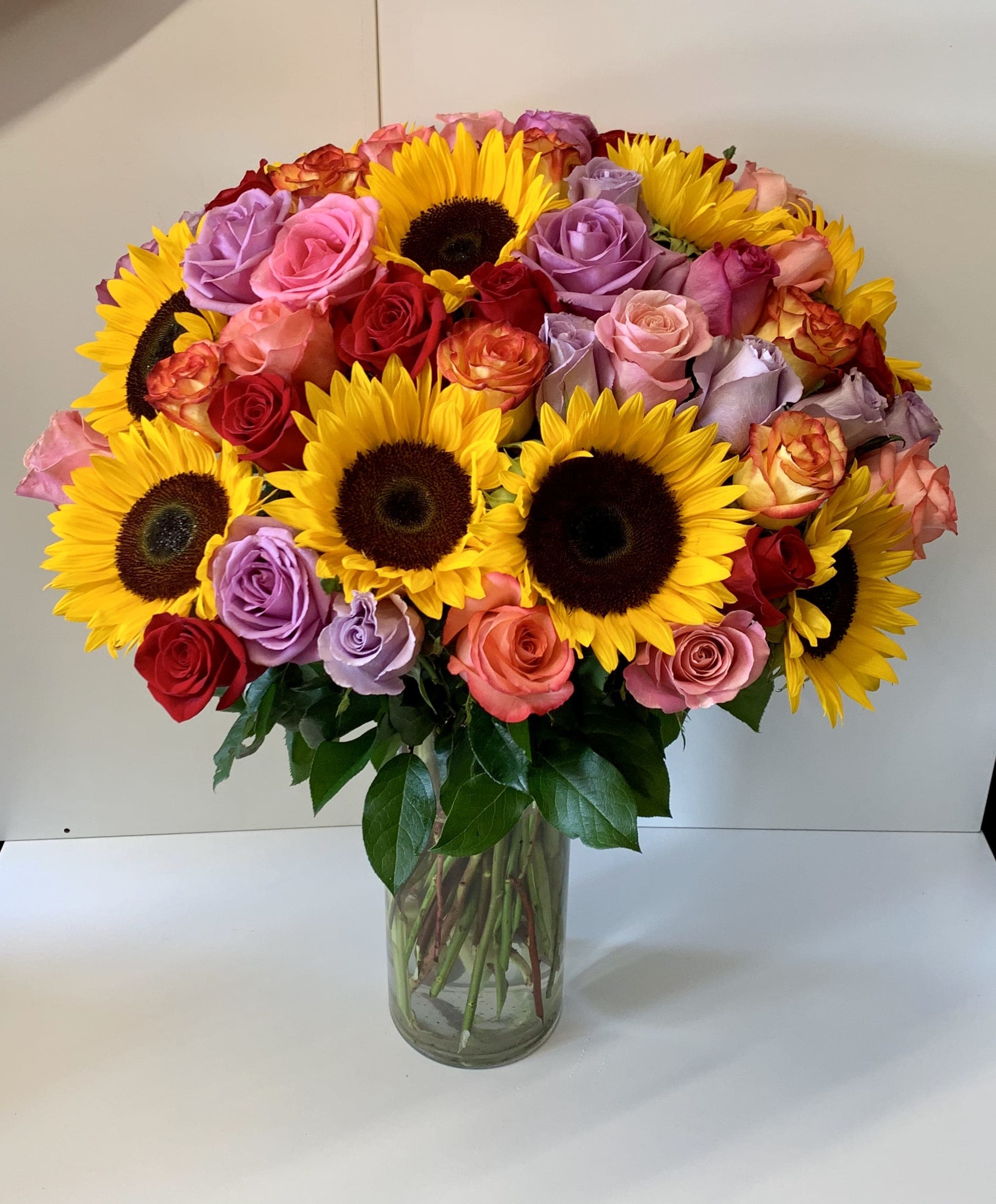 Tall glass vase of yellow sunflowers mixed with red, pink, and lavender roses