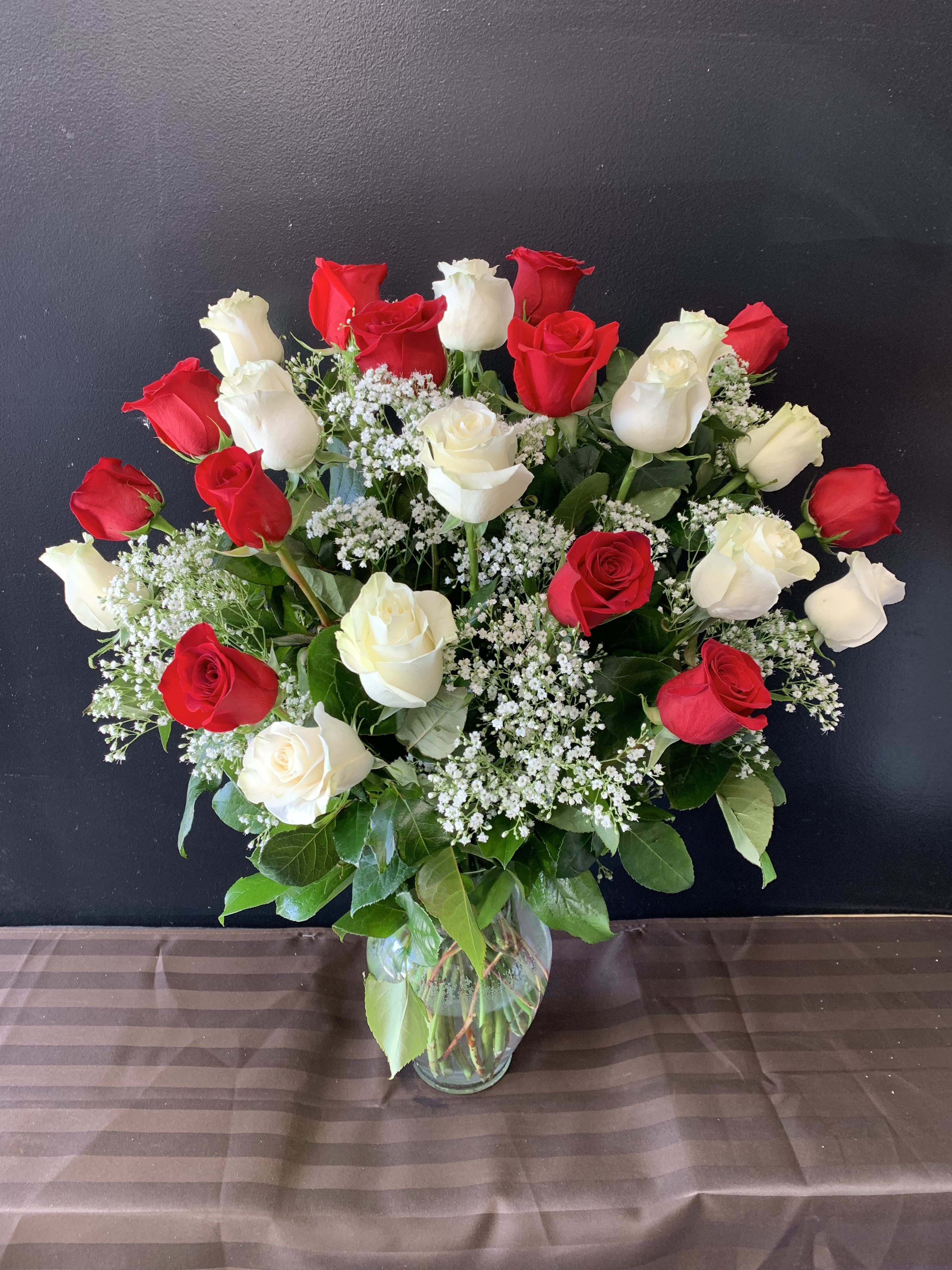 Tall arrangement of red and white roses with tiny white filler flowers in a clear glass vase