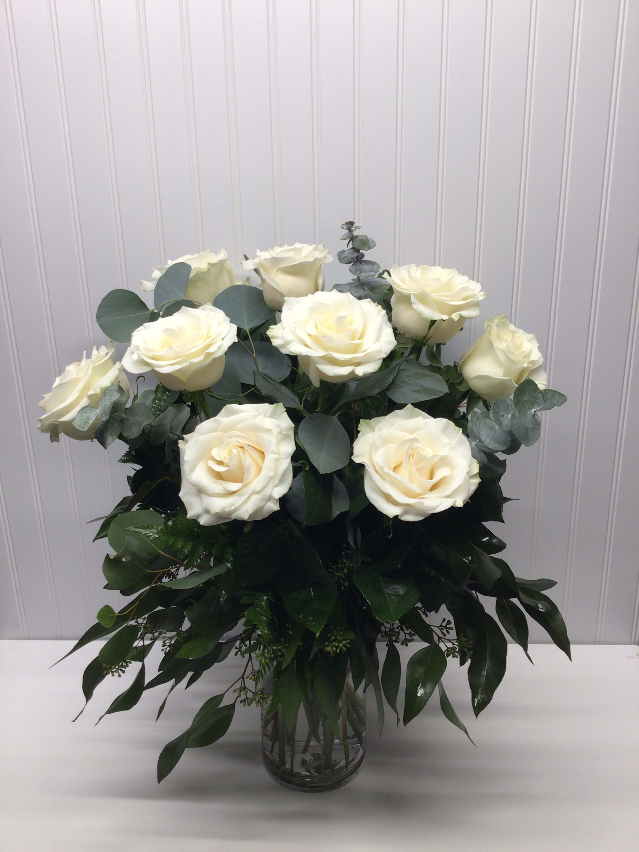 Tall arrangement of ivory roses with abundant greenery in a clear glass vase