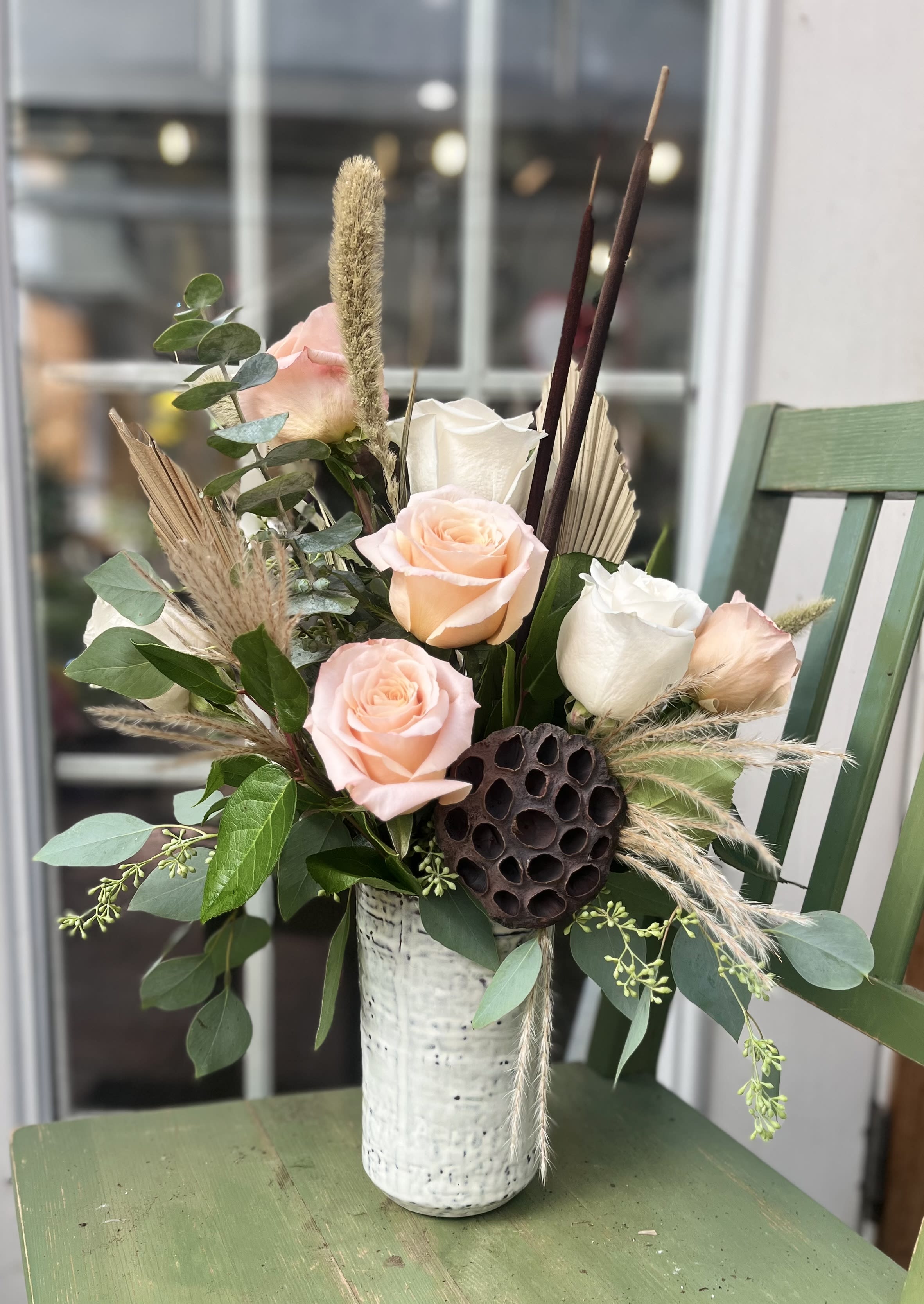 Peach and white roses with dried accents in a tall white ceramic vase