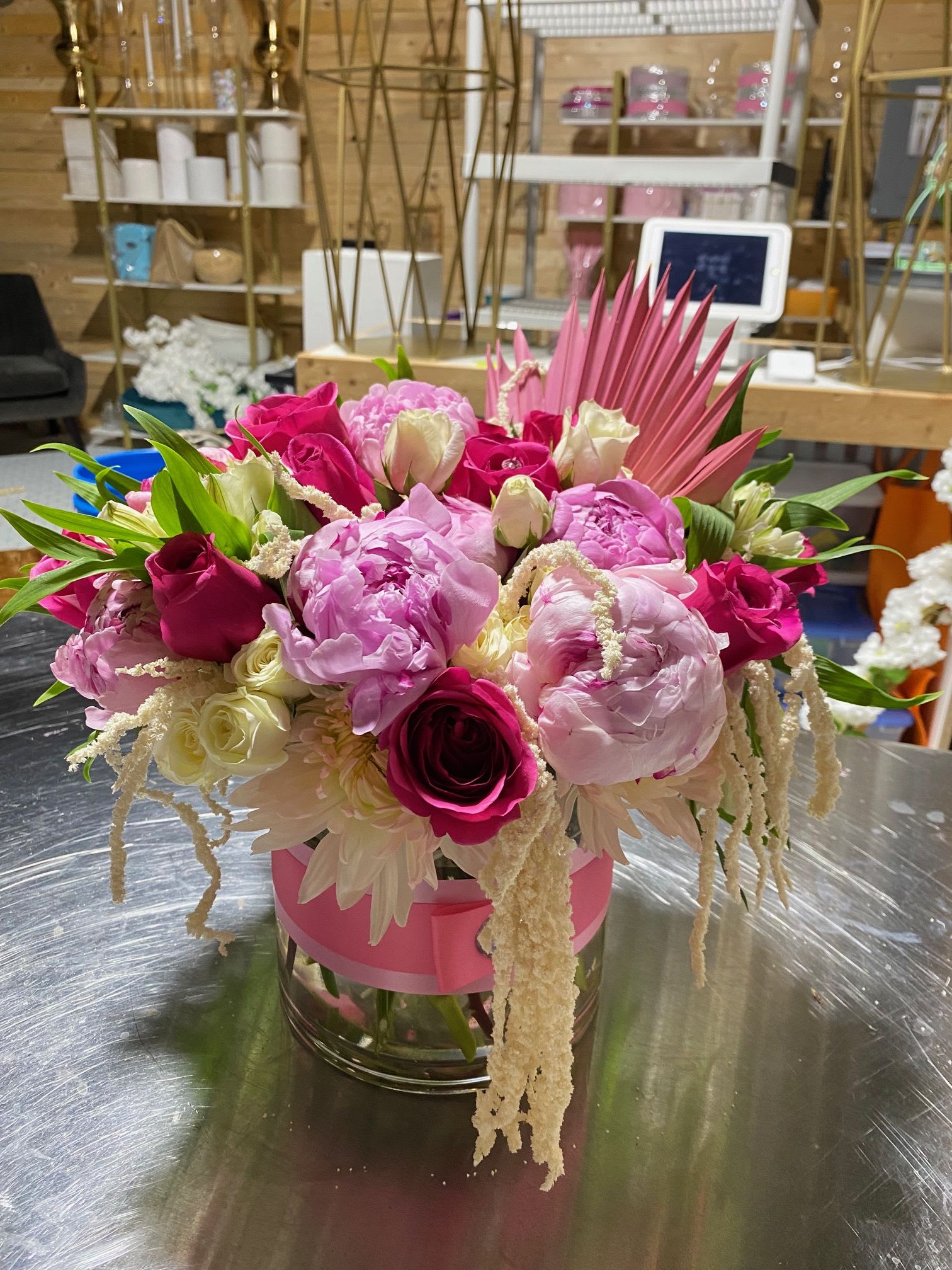 Low pink and white arrangement with peonies and roses in a glass vase wrapped with pink ribbon
