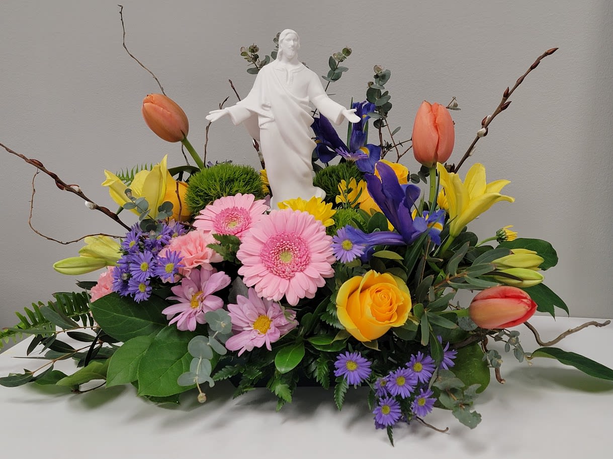 Resurrection Day Table Centerpiece - Spring flowers arranged around a white ceramic statue of Jesus, Gerbera daisies, tulips, daisies, roses, lilies, Iris, purple monte and an assortment of greenery.
