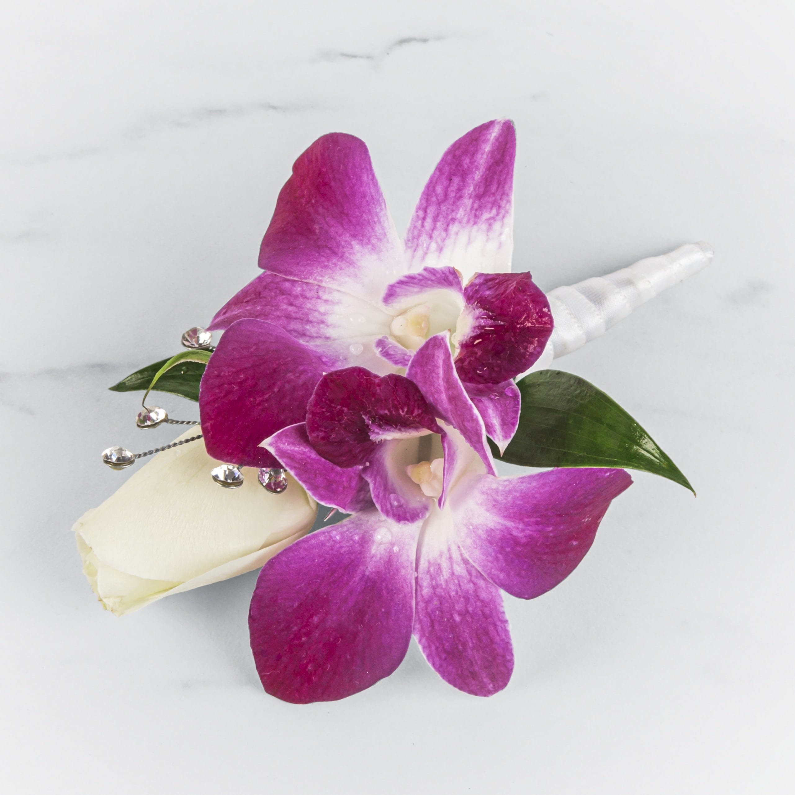Boutonniere with bright fuchsia orchids and a single white rosebud with jeweled accents.