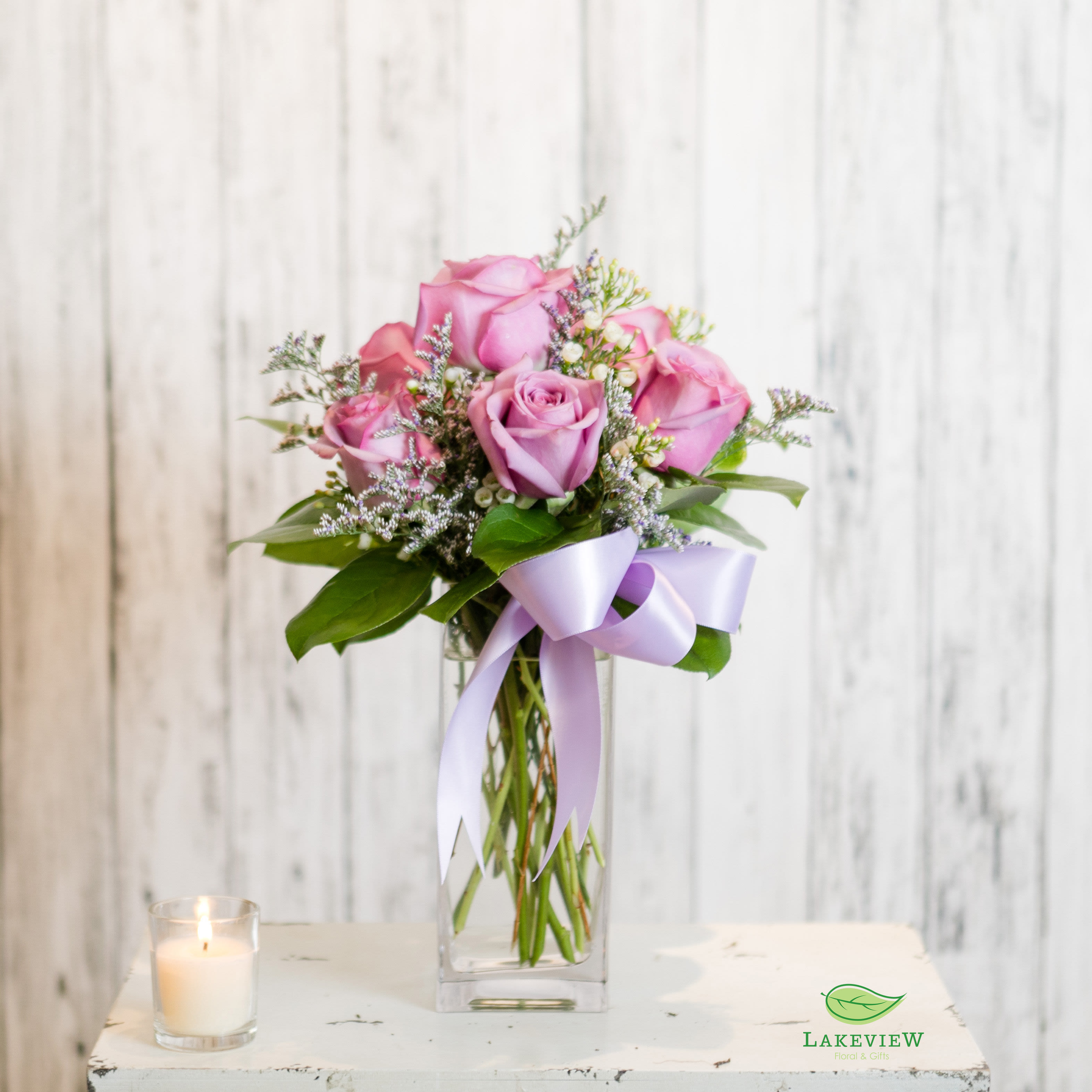 Pink roses in a clear glass vase with a lavender ribbon and candle