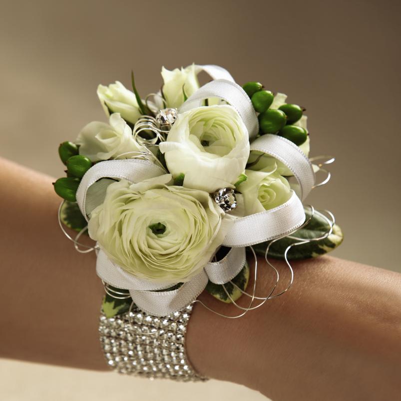  White Exquisite Wedding Corsage - White Wedding Corsage is a sweet display of wedding day  elegance. White ranunculus and spray roses are brought together with  green hypericum berries and arranged exquisitely on a sparkling flower  bracelet. Accented with a white taffeta ribbon, this corsage is perfect  for any member of the wedding party. Approx. 4-inches in diameter. 