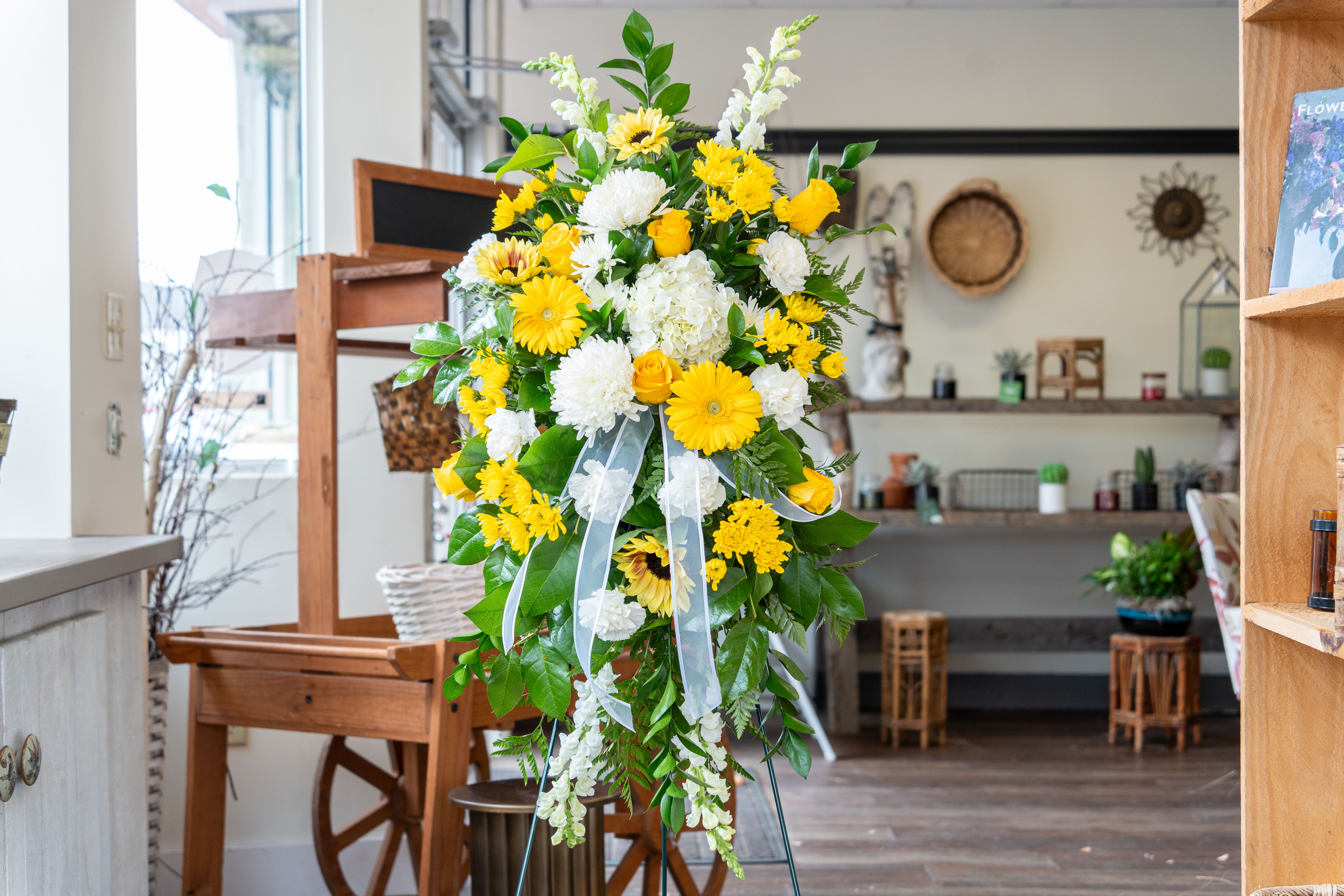 Forever Bright - And easel arrangement featuring yellow gerber daisy's, yellow roses, sunflowers, yellow cremon, white mums, white hydrangea, white snapdragons, and white carnations with mixed greens to fulfill this beautiful piece. Reminder that the colors and flower types can be changed to different colors and to accommodate your budget. Contact us to discuss these changes.
