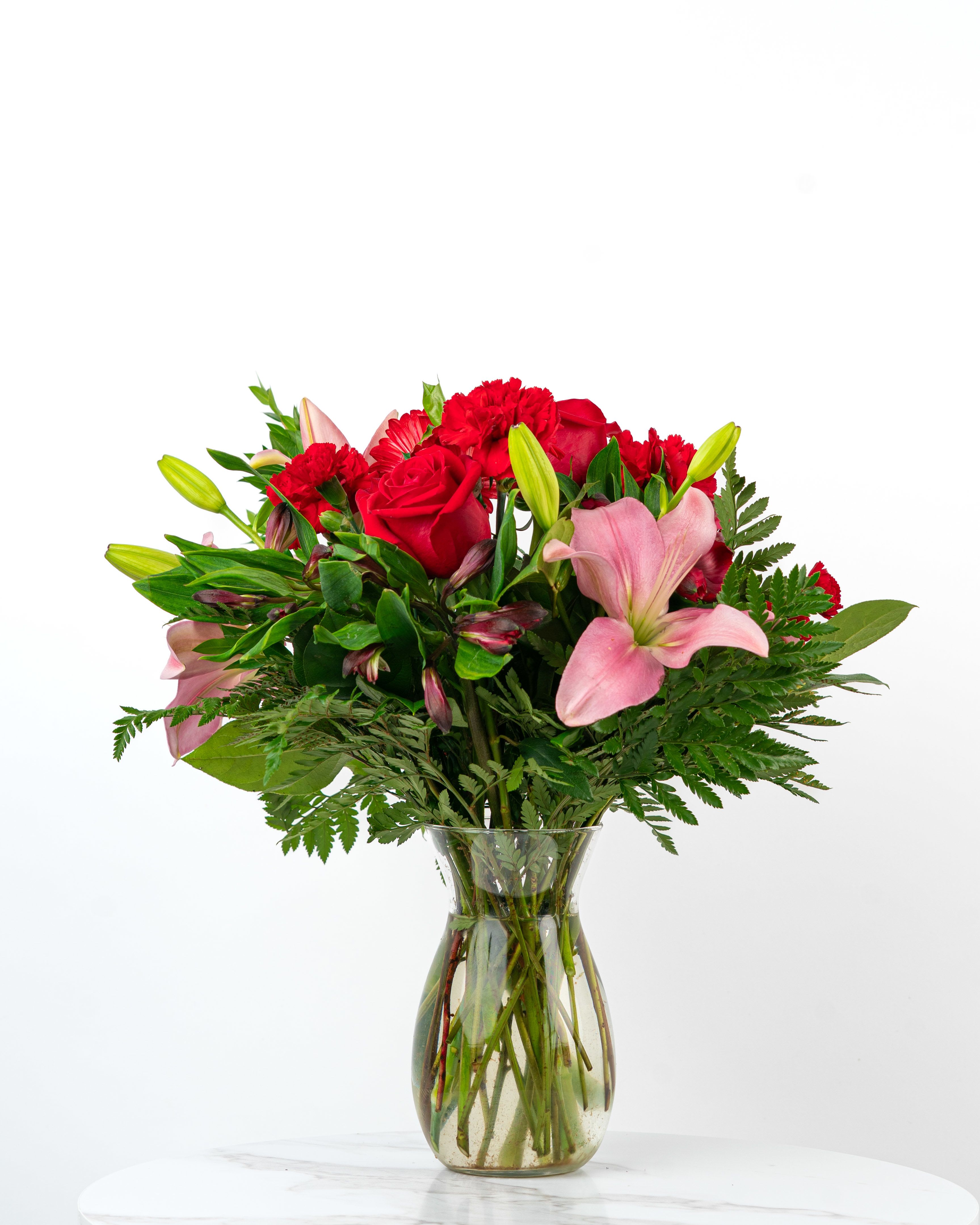 Bouquet of red roses, pink lilies, and red carnations in a glass vase